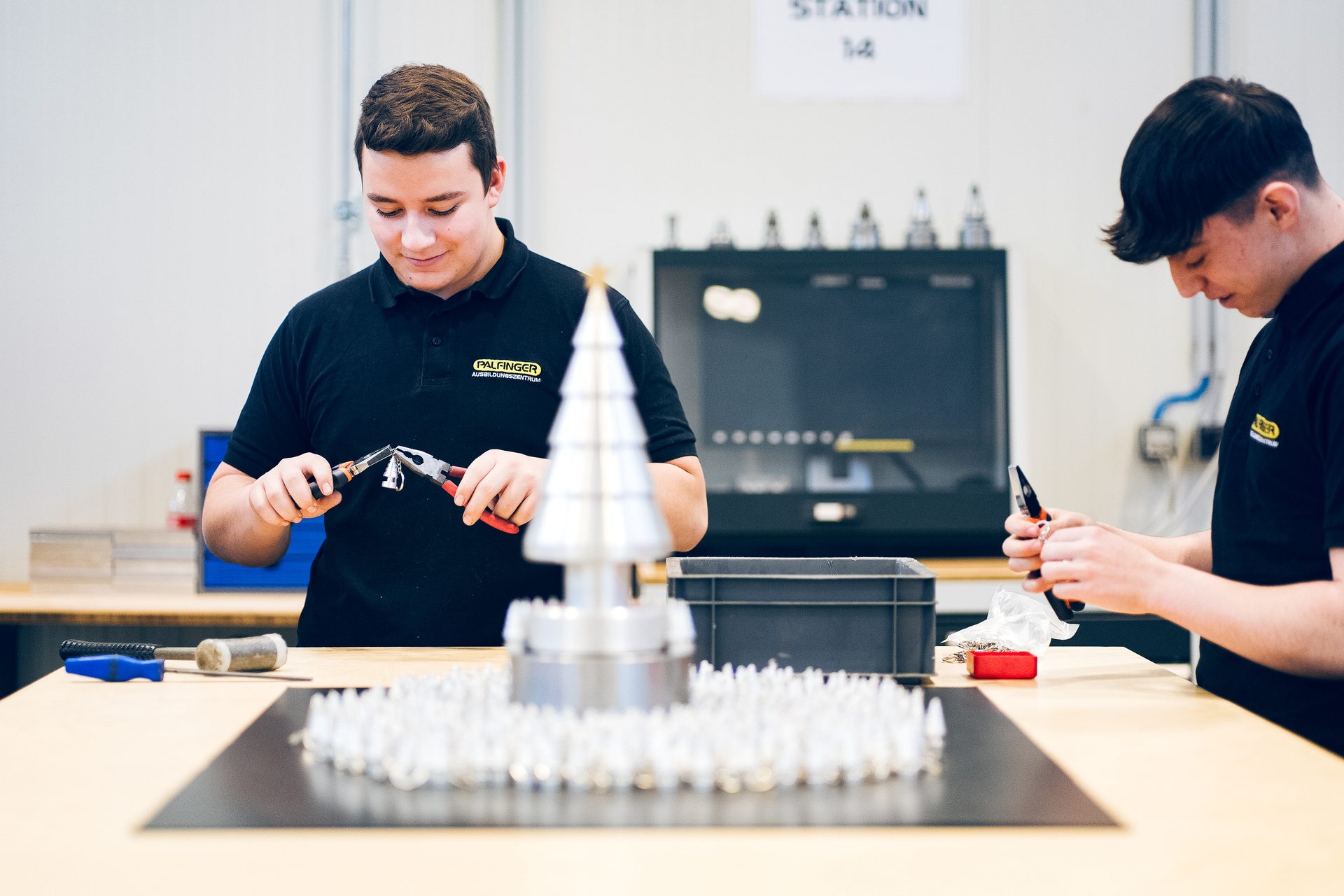 Two young men assemble a metallic Christmas tree with tools in a workshop.