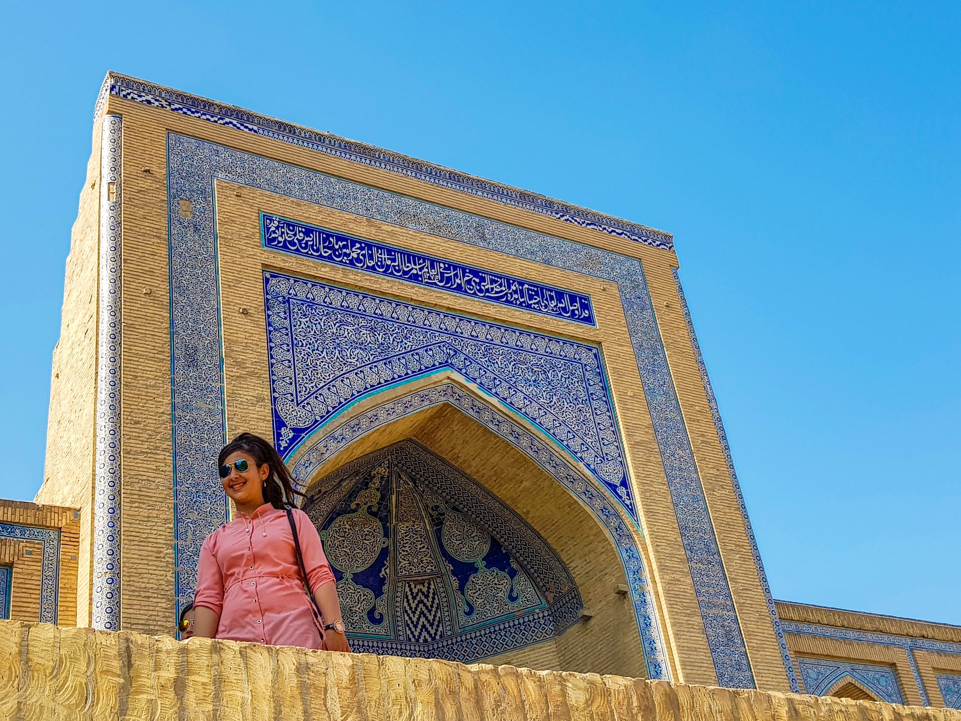 A woman smiles in front of a majestic, blue-tiled building against a clear sky.