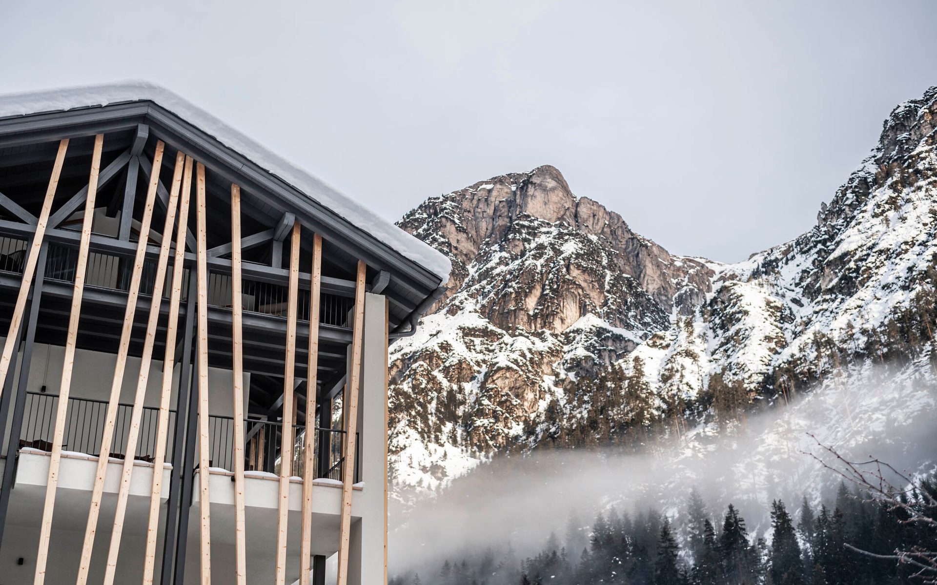 Modern building with snow-covered roof, set against misty, snow-capped mountains.