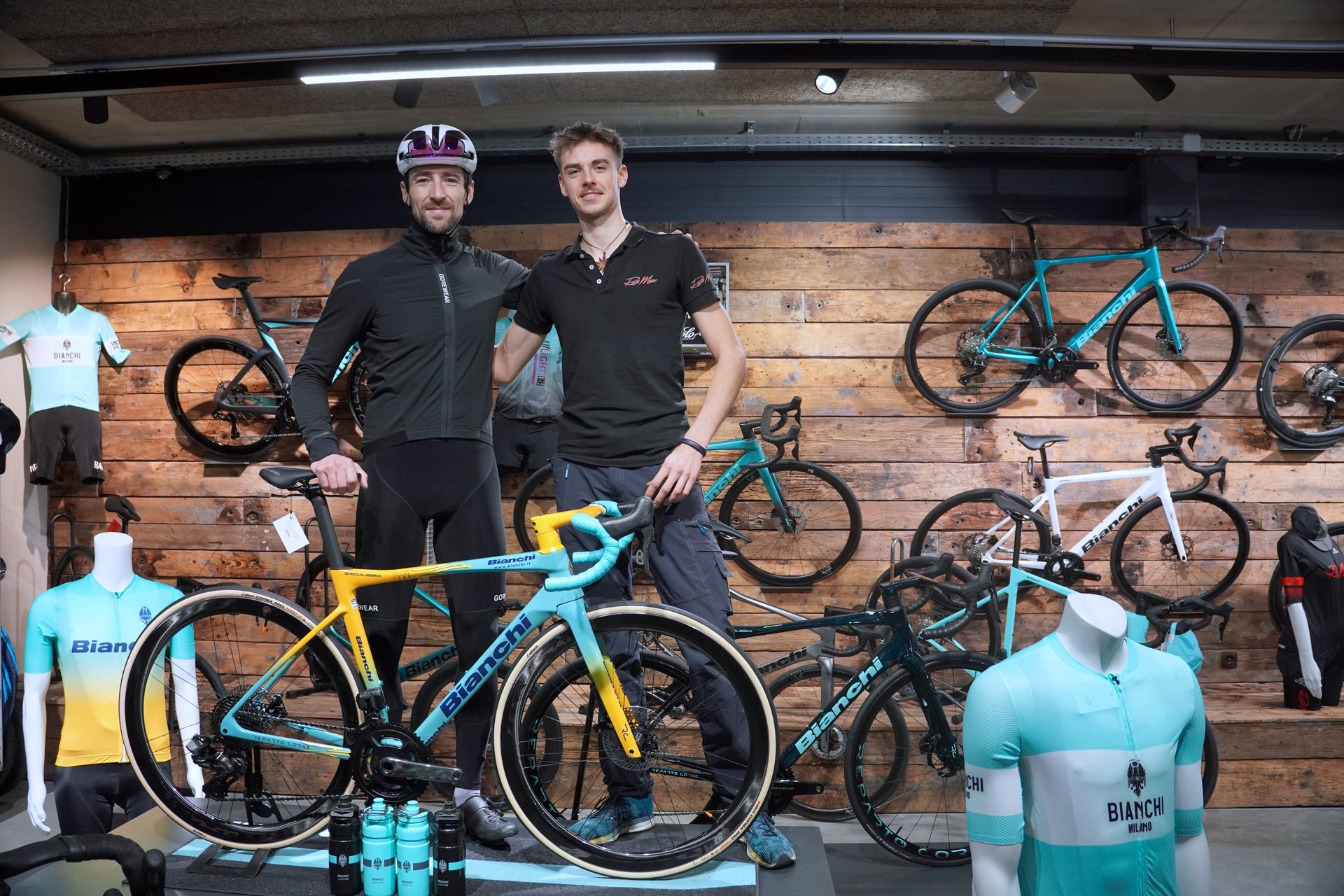 Two men, one a cyclist, stand with a yellow and blue Bianchi bicycle in a bike shop.