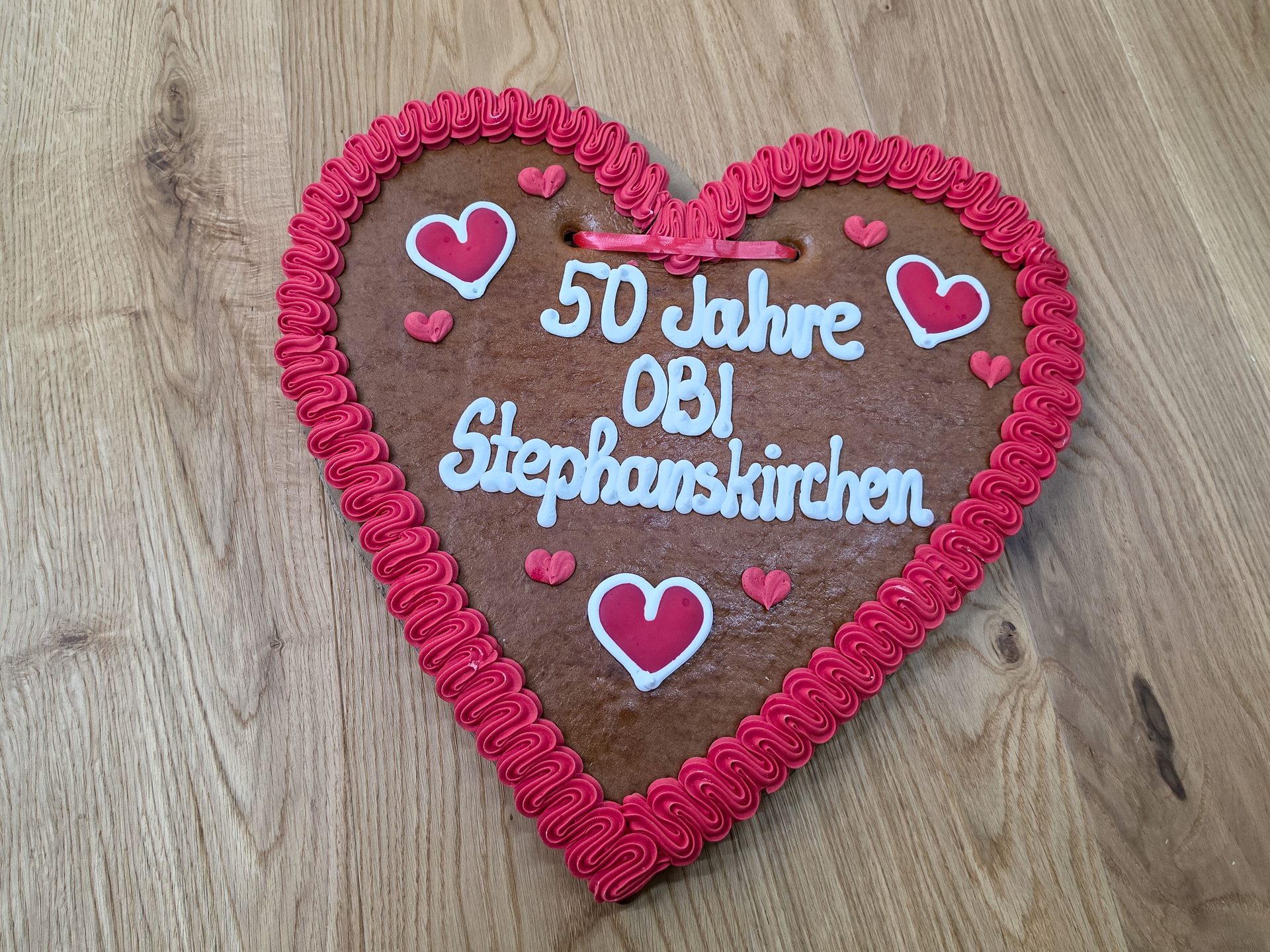 A heart-shaped gingerbread cookie with red icing border and white text "50 Jahre OBI Stephanskirchen".