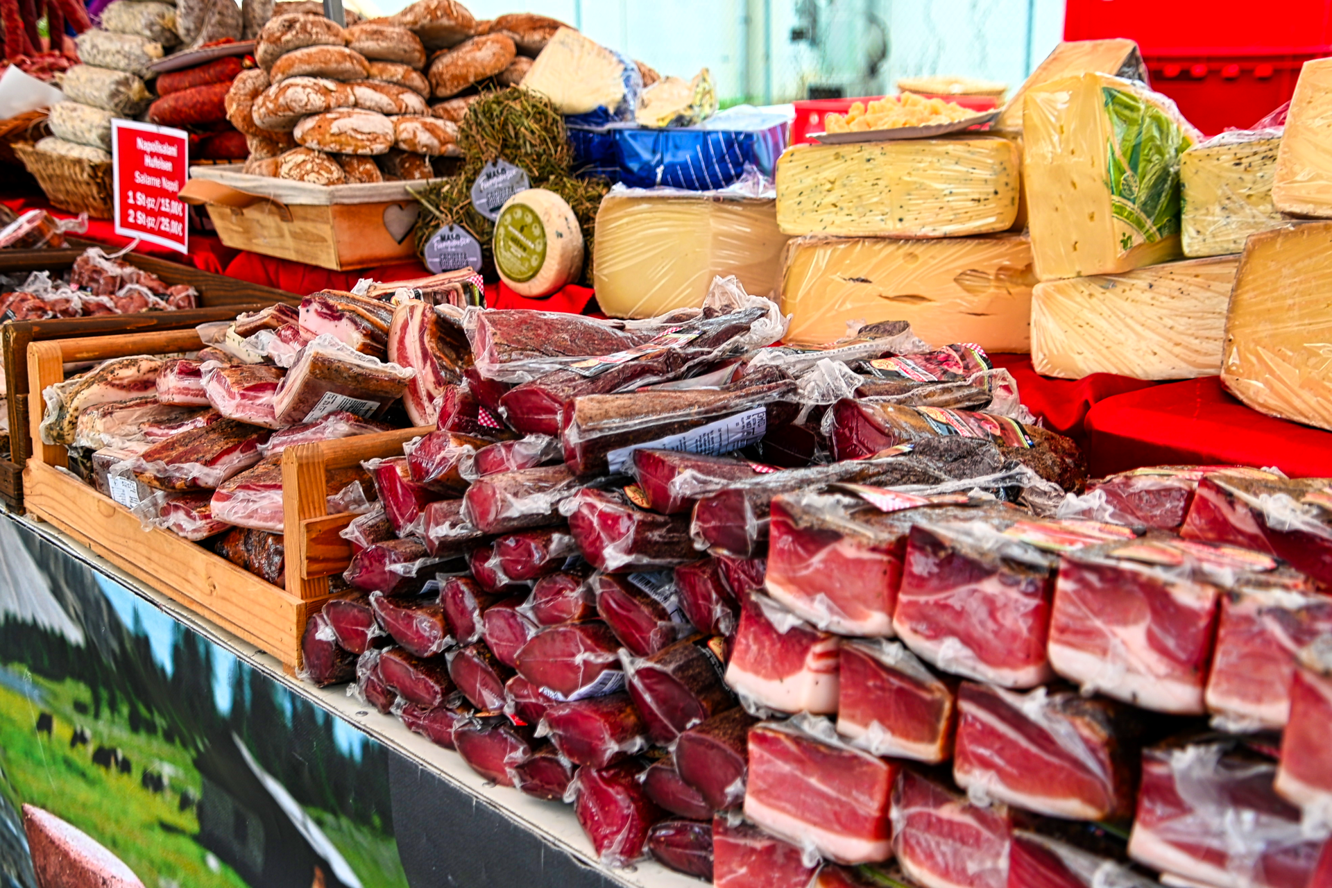 A market stall packed with cured meats, various cheeses, and fresh bread for sale.