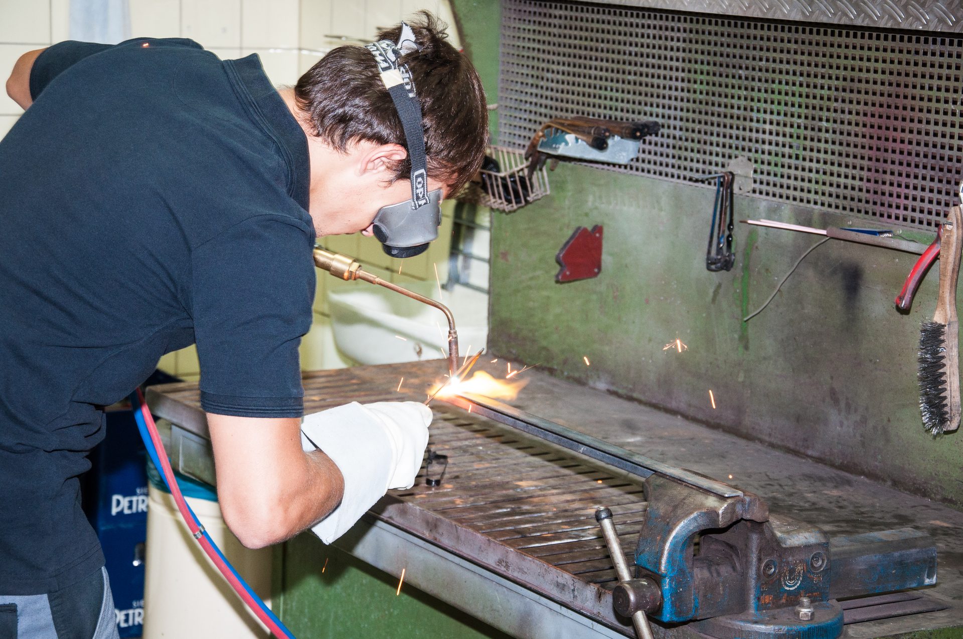 A person welds metal with a torch, wearing safety goggles and gloves, sparks flying.