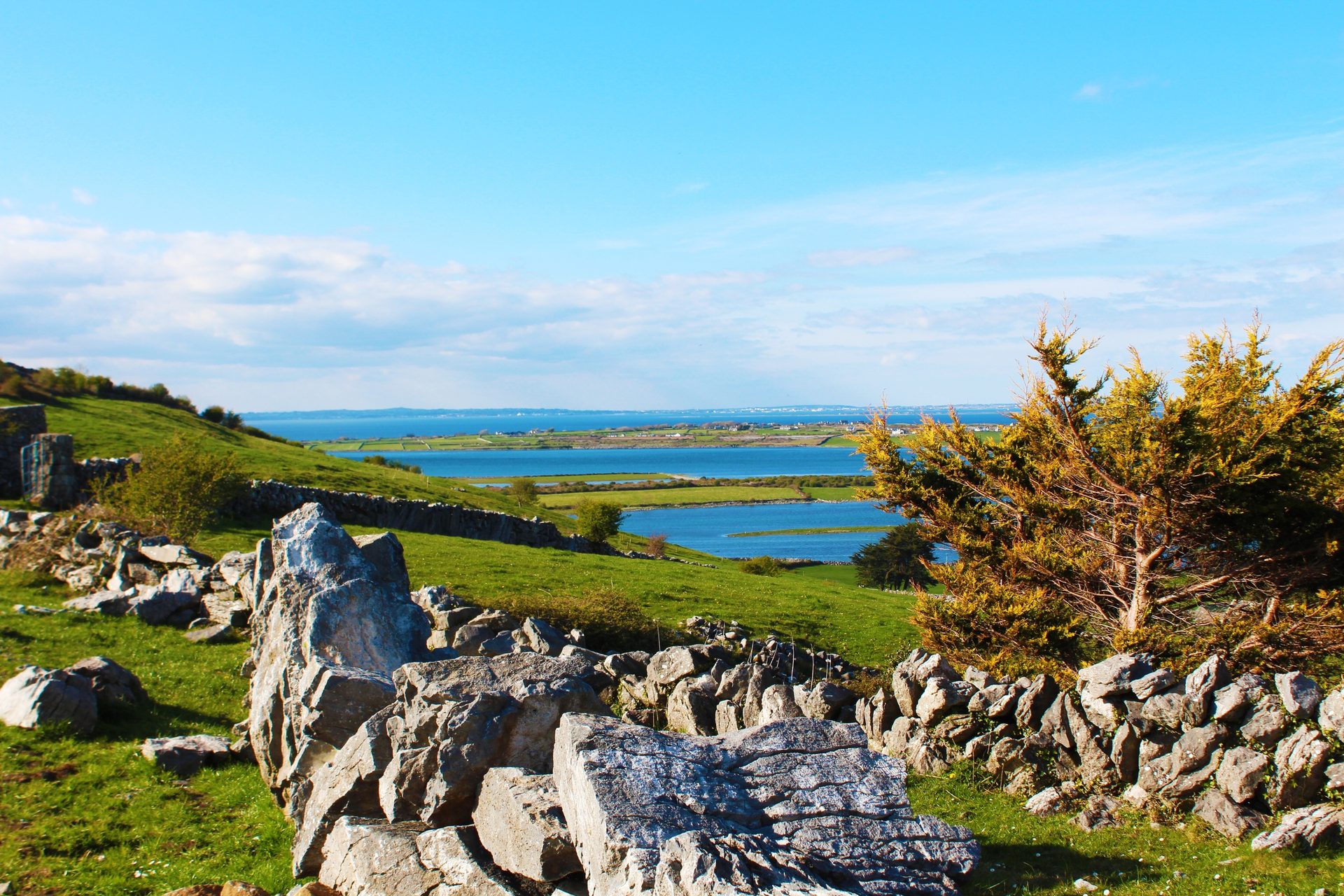Green hills, ancient stone walls, and a blue bay under a bright sky in the Irish countryside.