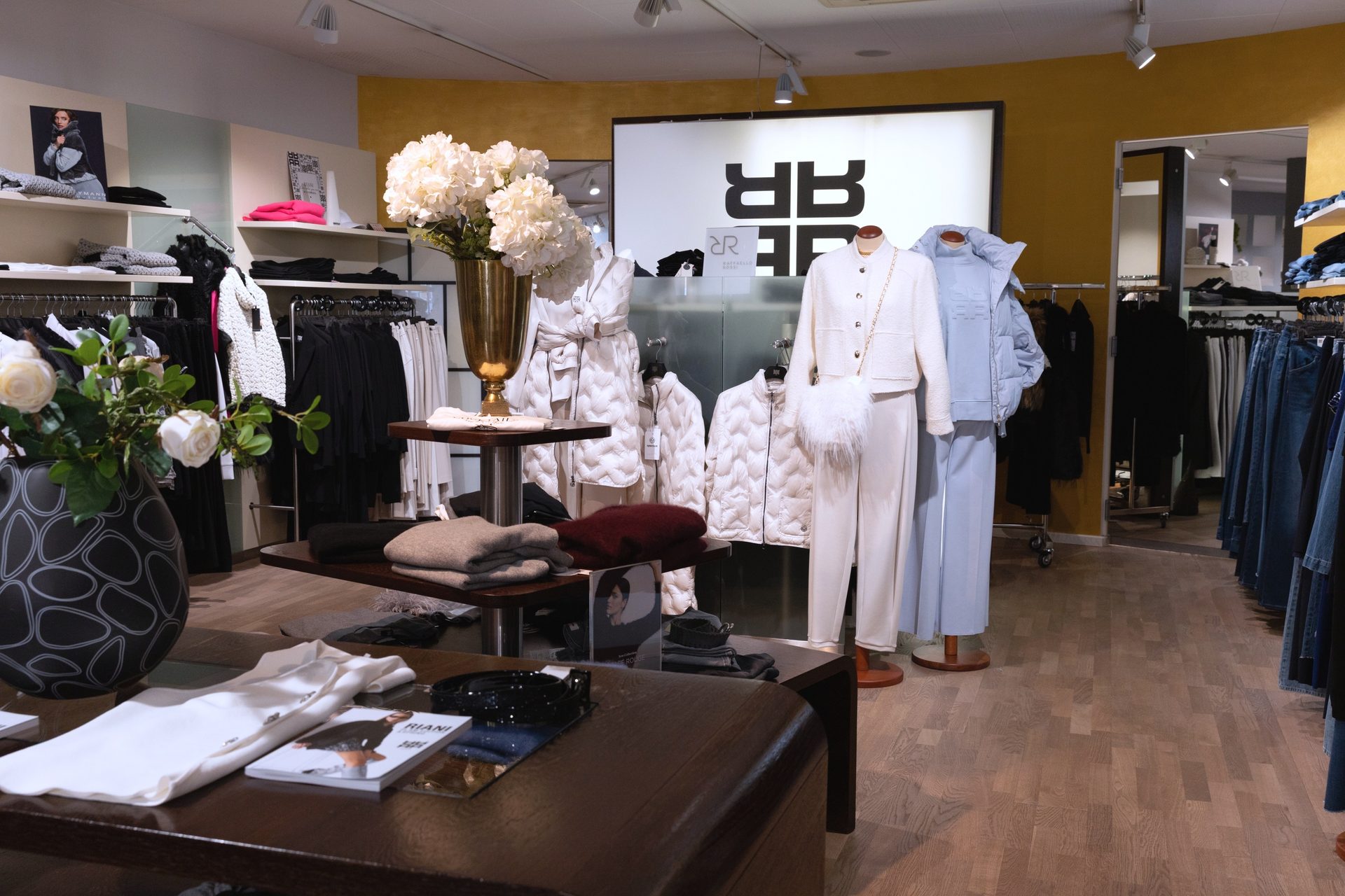 Stylish clothing store interior with mannequins, clothing racks, display tables, and an "RR" logo.