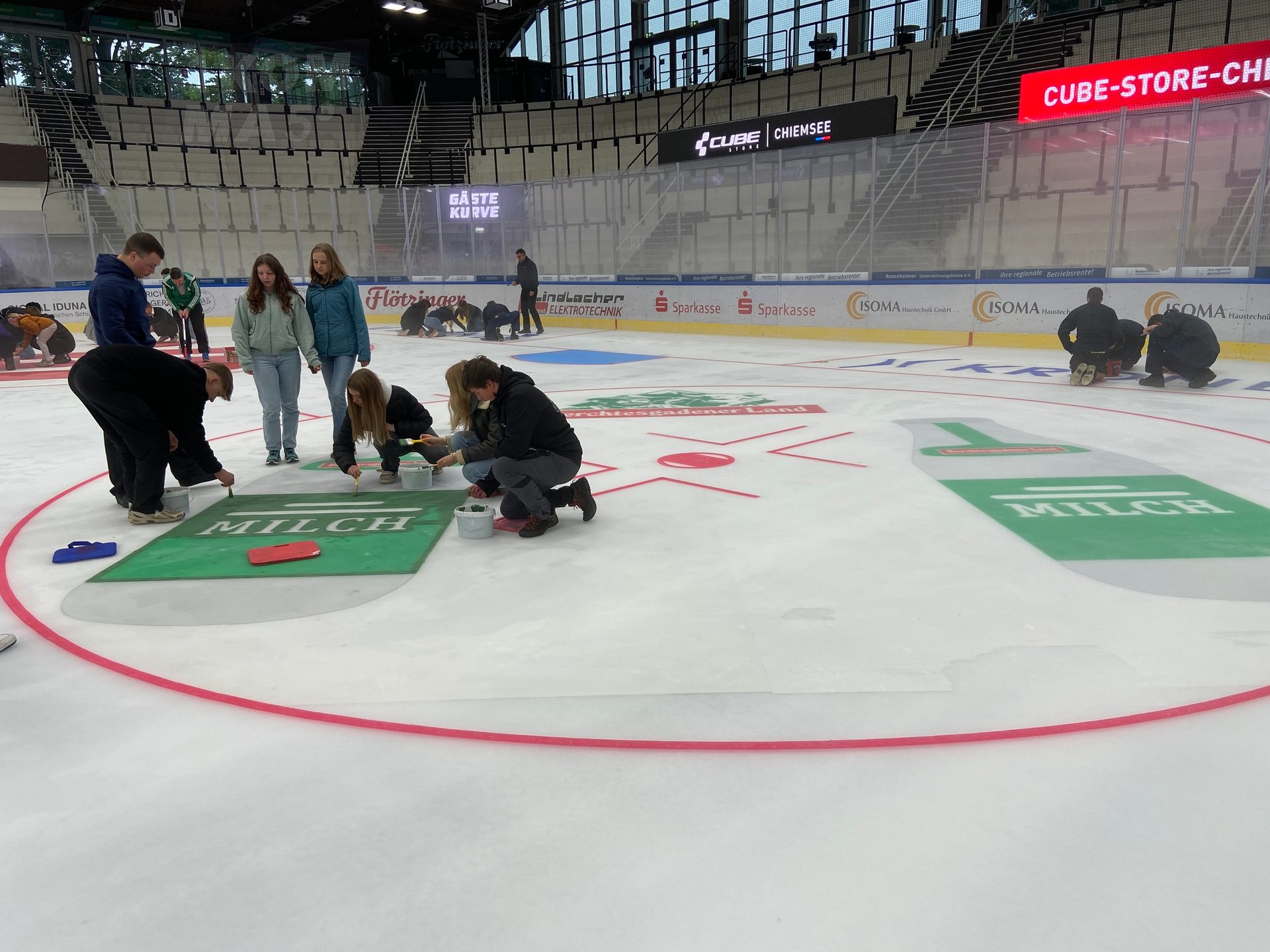 People painting logos and graphics on an ice rink in an arena.