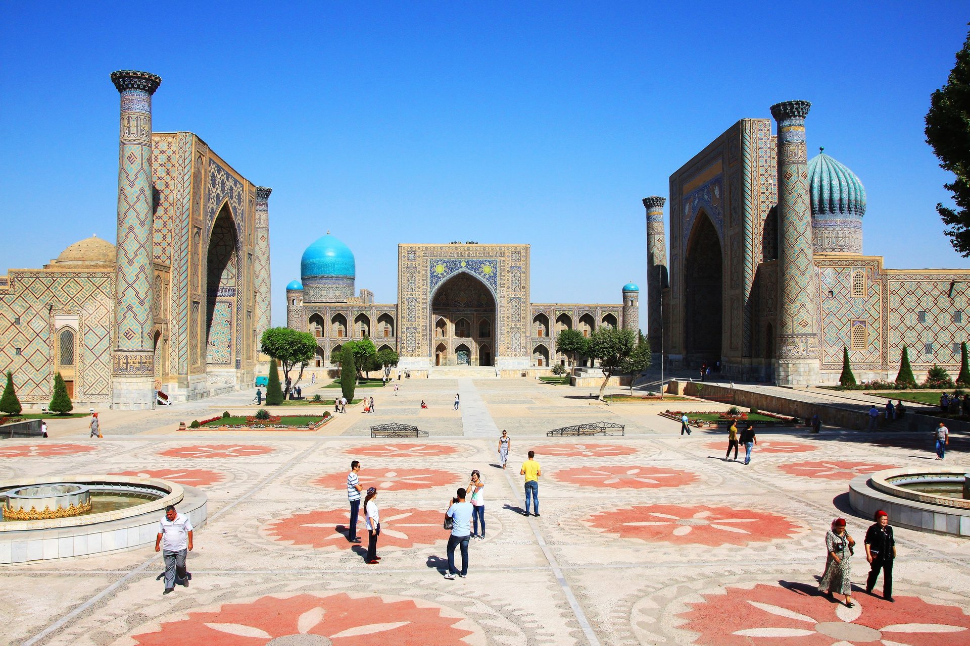 Registan Square in Samarkand with three grand madrasahs, intricate tilework, and people walking.