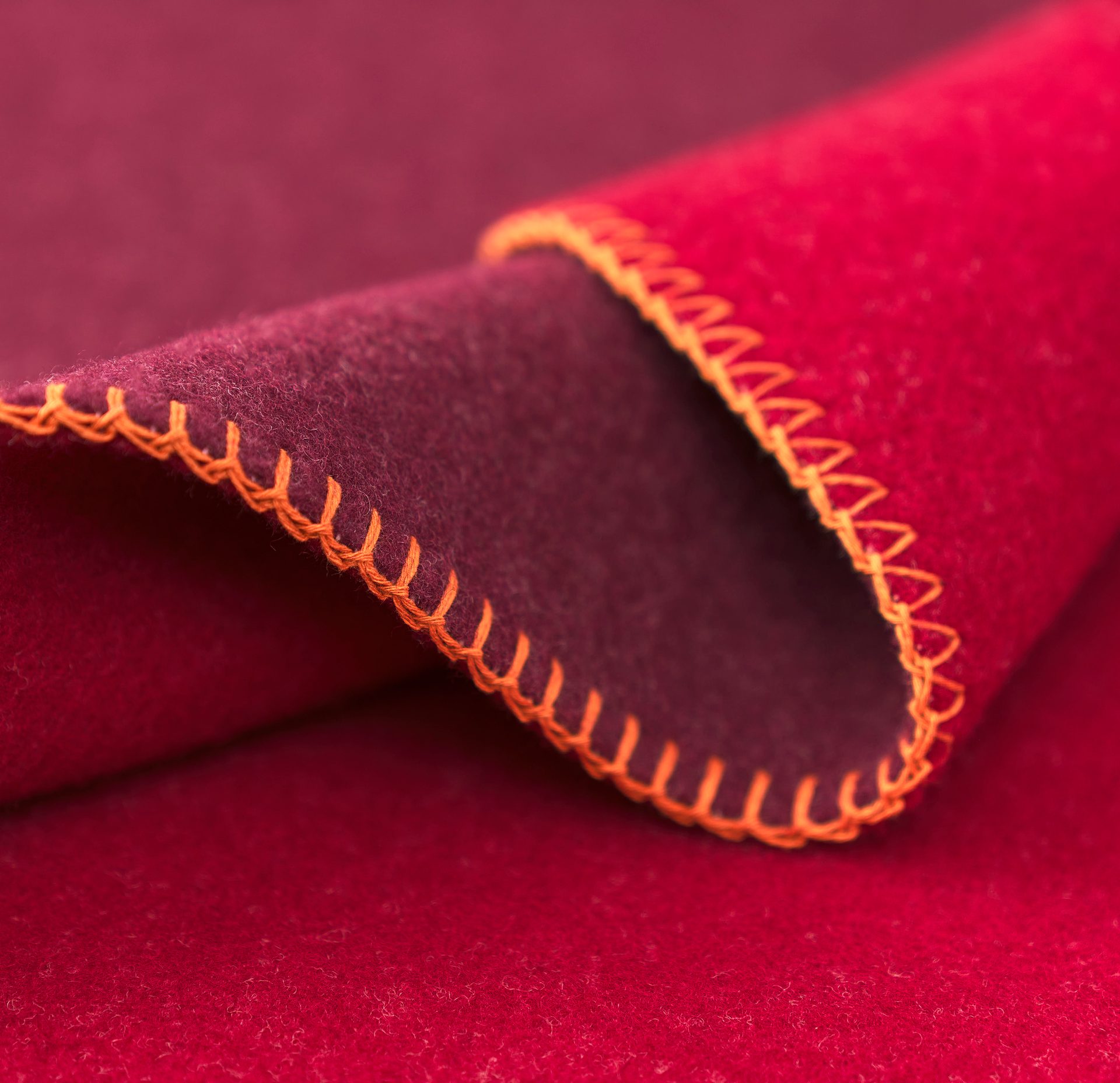 Folded deep red fabric with a darker red underside and bright orange blanket stitching.