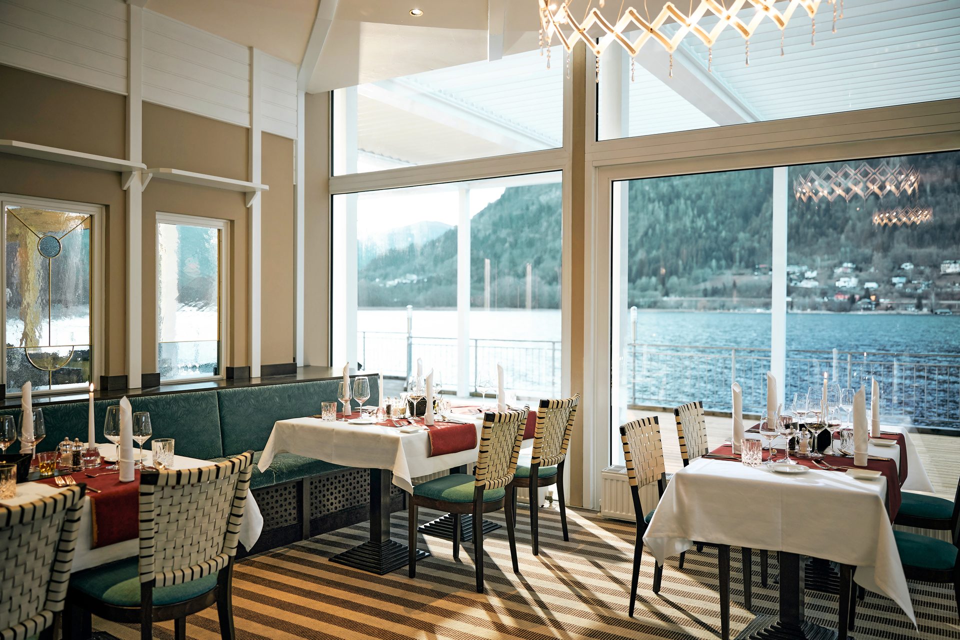 Elegant restaurant with tables set by large windows overlooking a scenic lake and mountains.
