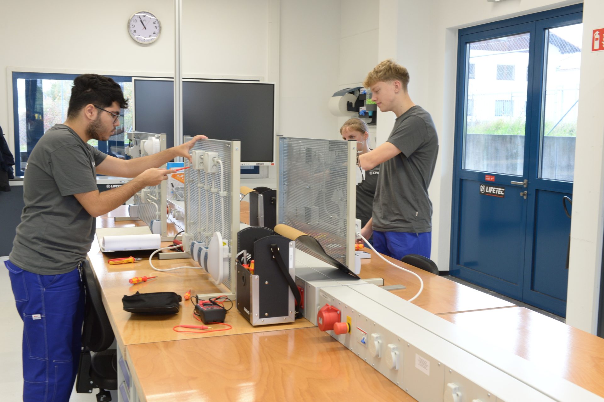 Three students in an electrical lab assembling components on training boards.