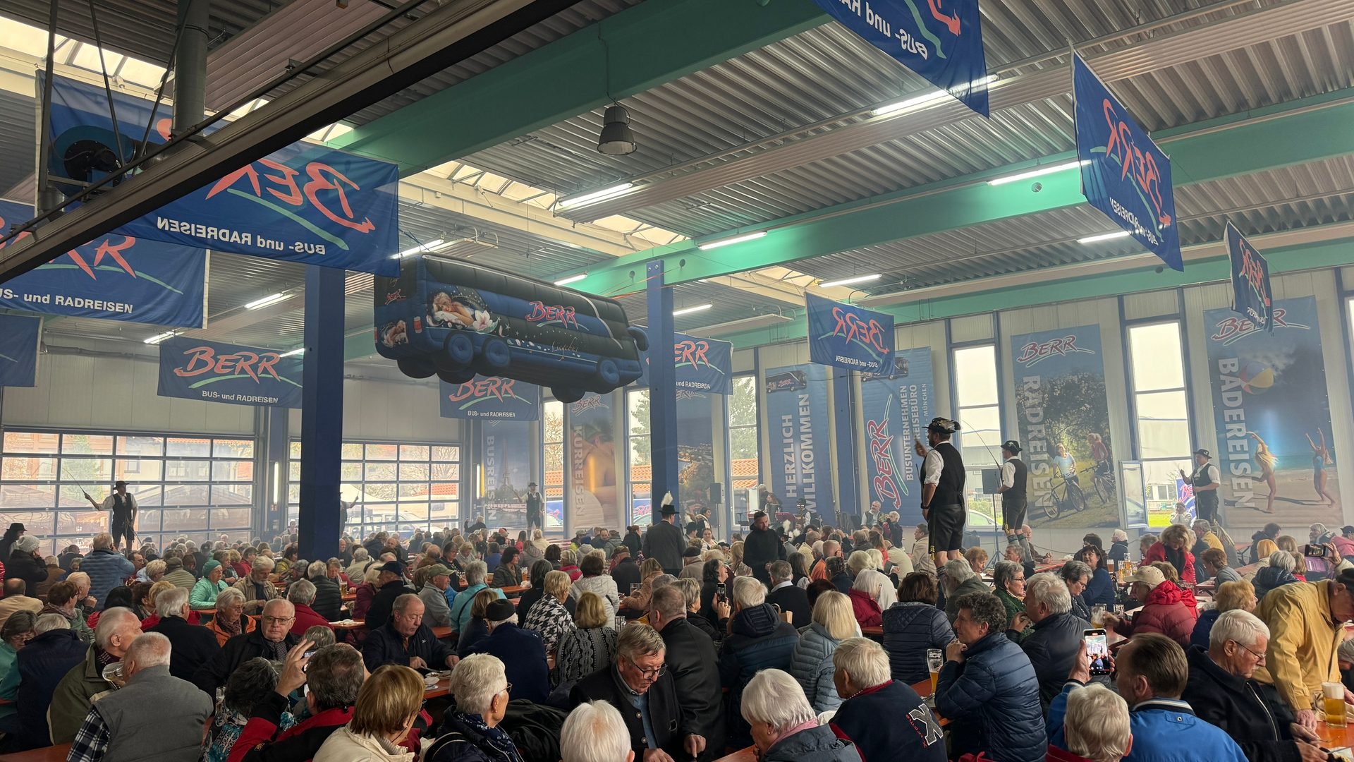 Large indoor event with many attendees, travel banners, an inflatable bus, and performers.