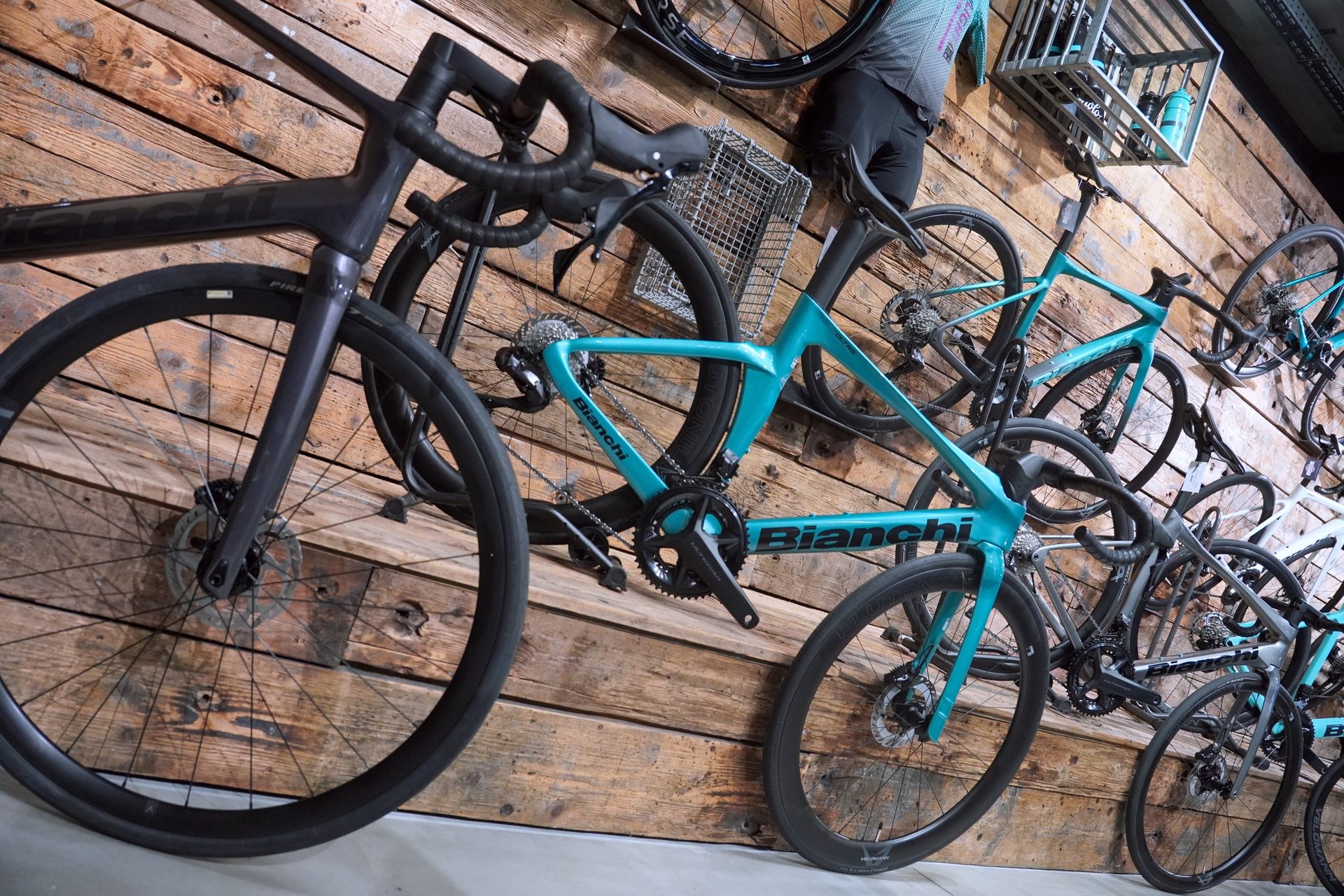 Multiple road bikes, including teal Bianchi models, displayed artistically on a rustic wooden wall.