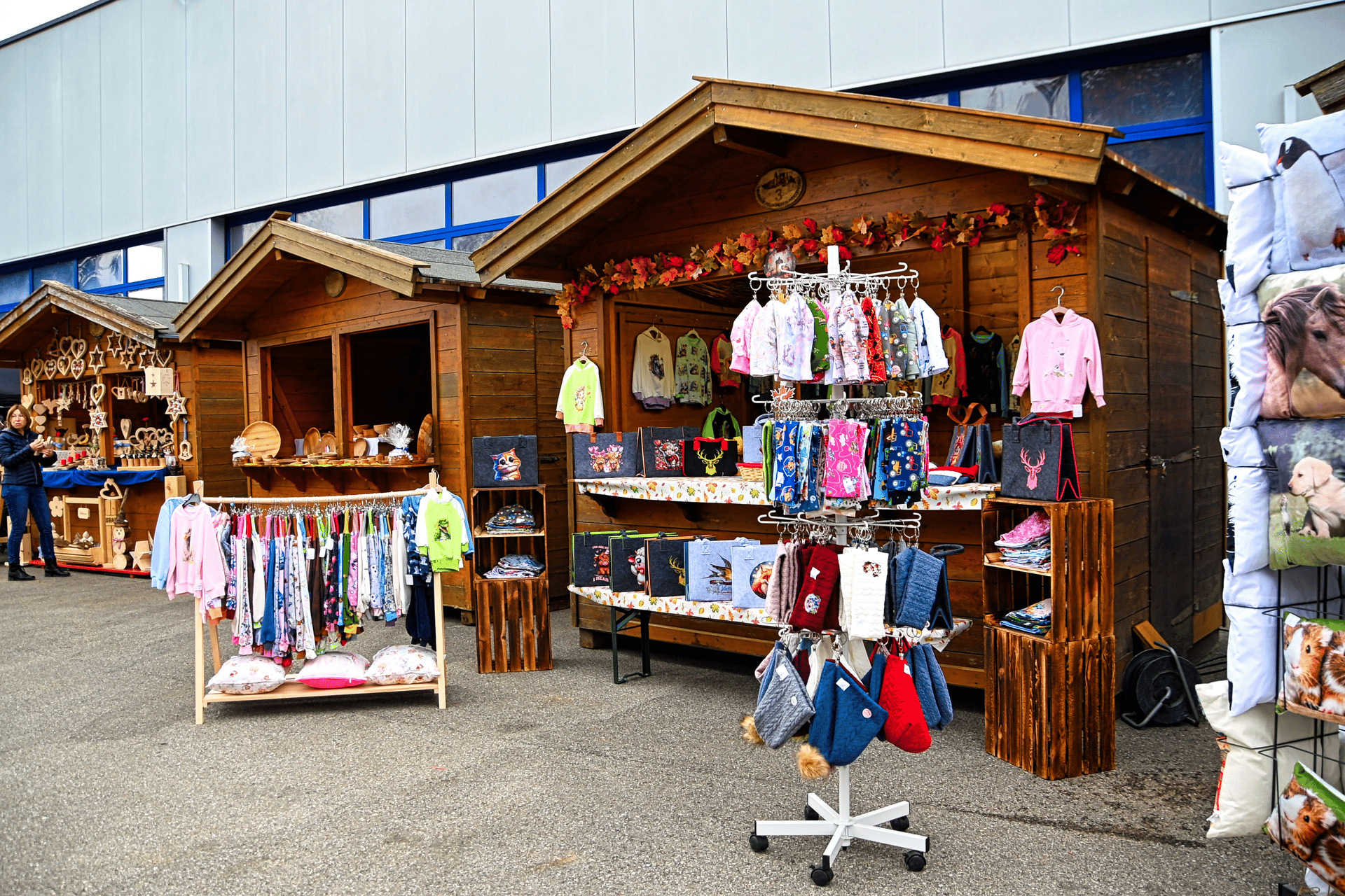 Rustic wooden stalls at an outdoor market displaying colorful clothes, handcrafted wooden goods, and animal-themed pillows.
