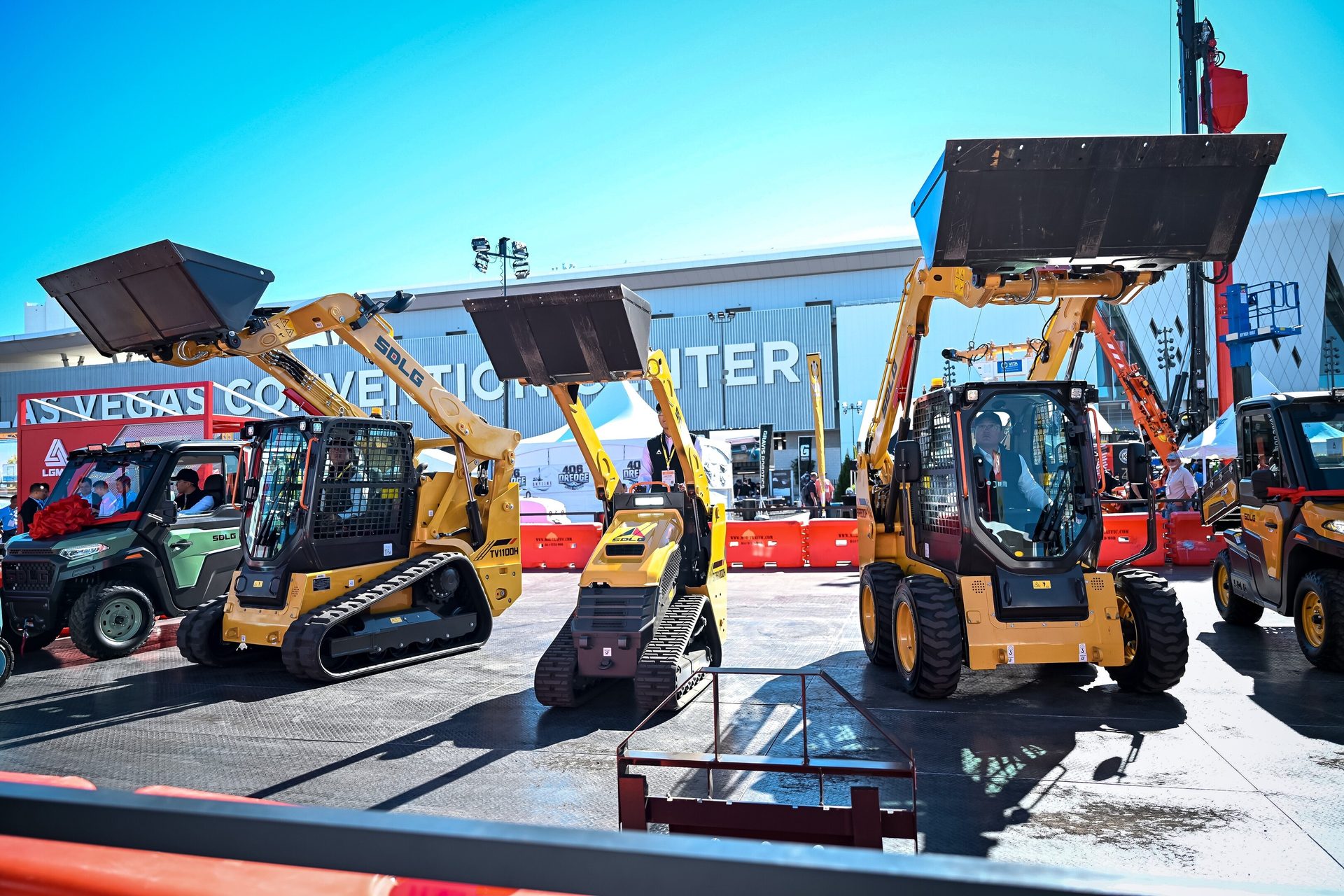 Three yellow SDLG skid steer loaders, two tracked and one wheeled, displayed at a convention center.