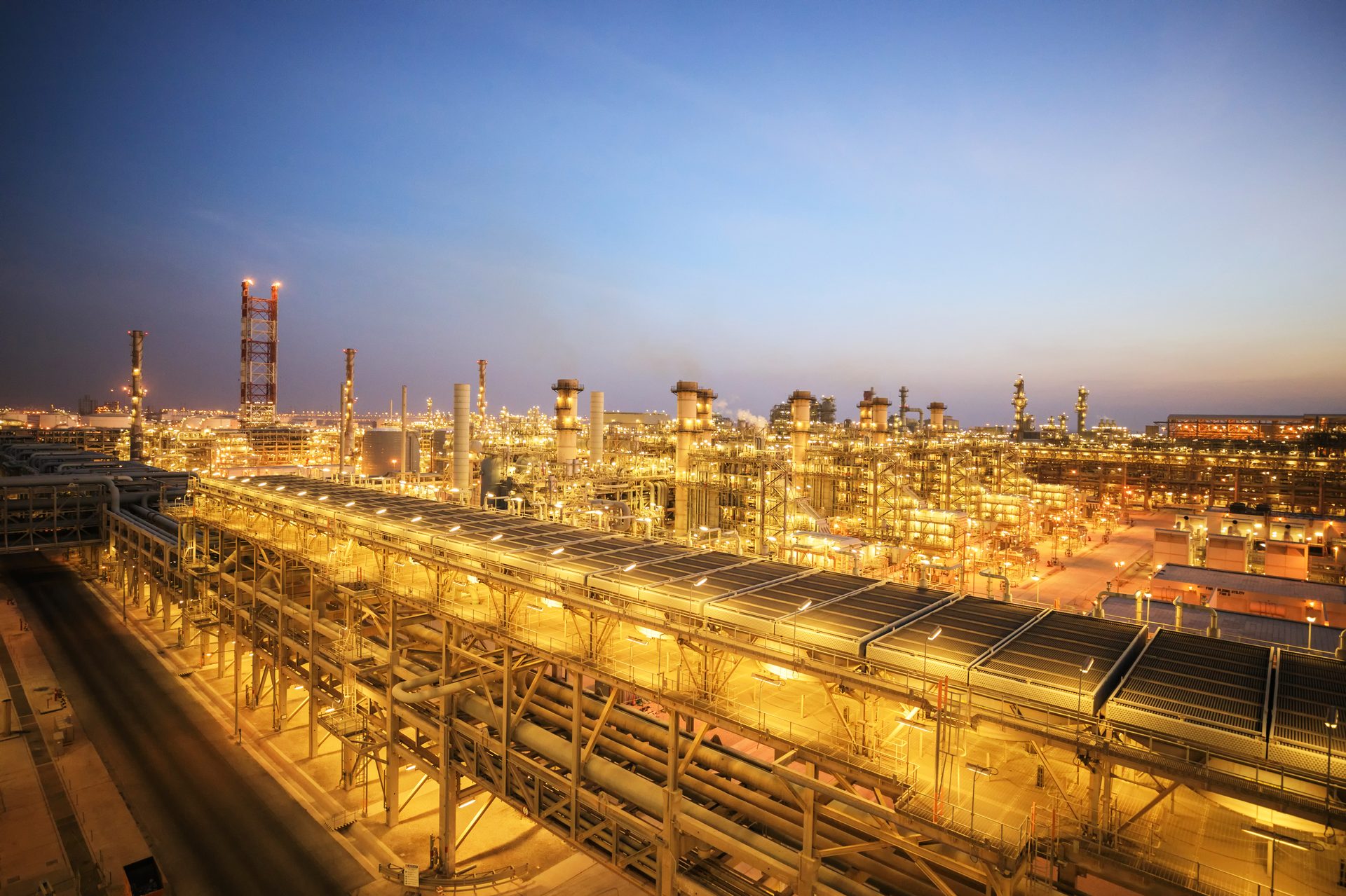 Aerial view of a sprawling industrial complex, brilliantly illuminated at dusk under a blue sky.