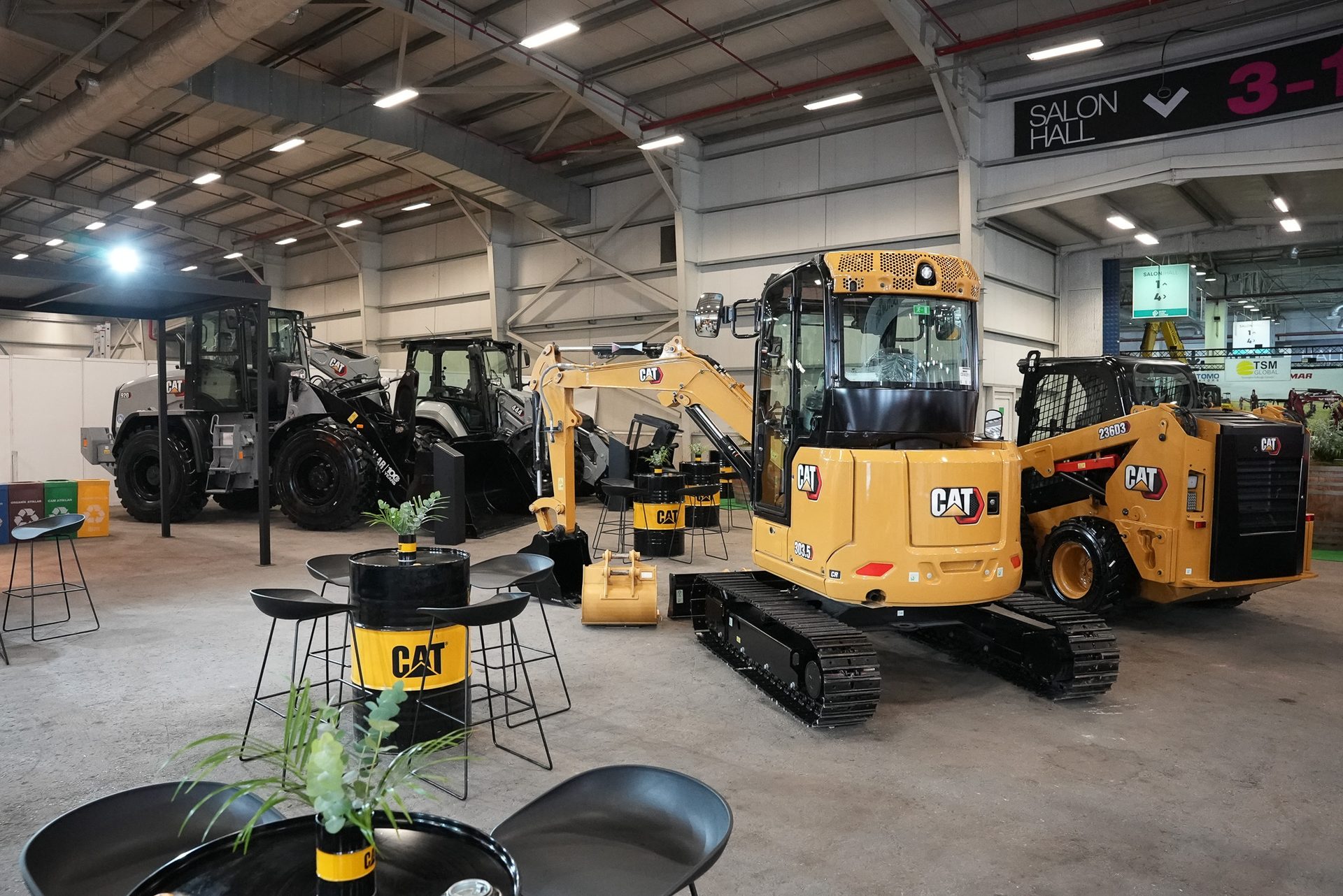 Indoor CAT equipment display with excavators, loaders, and branded seating at a trade show.