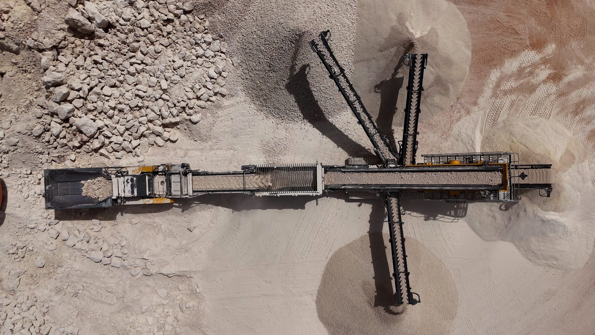 Aerial view of a rock crusher and sorter creating gravel piles.