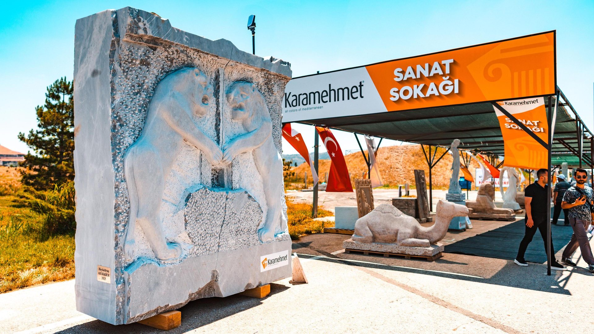 Outdoor art exhibit with a large marble sculpture, other sculptures, and "SANAT SOKAĞI" sign.