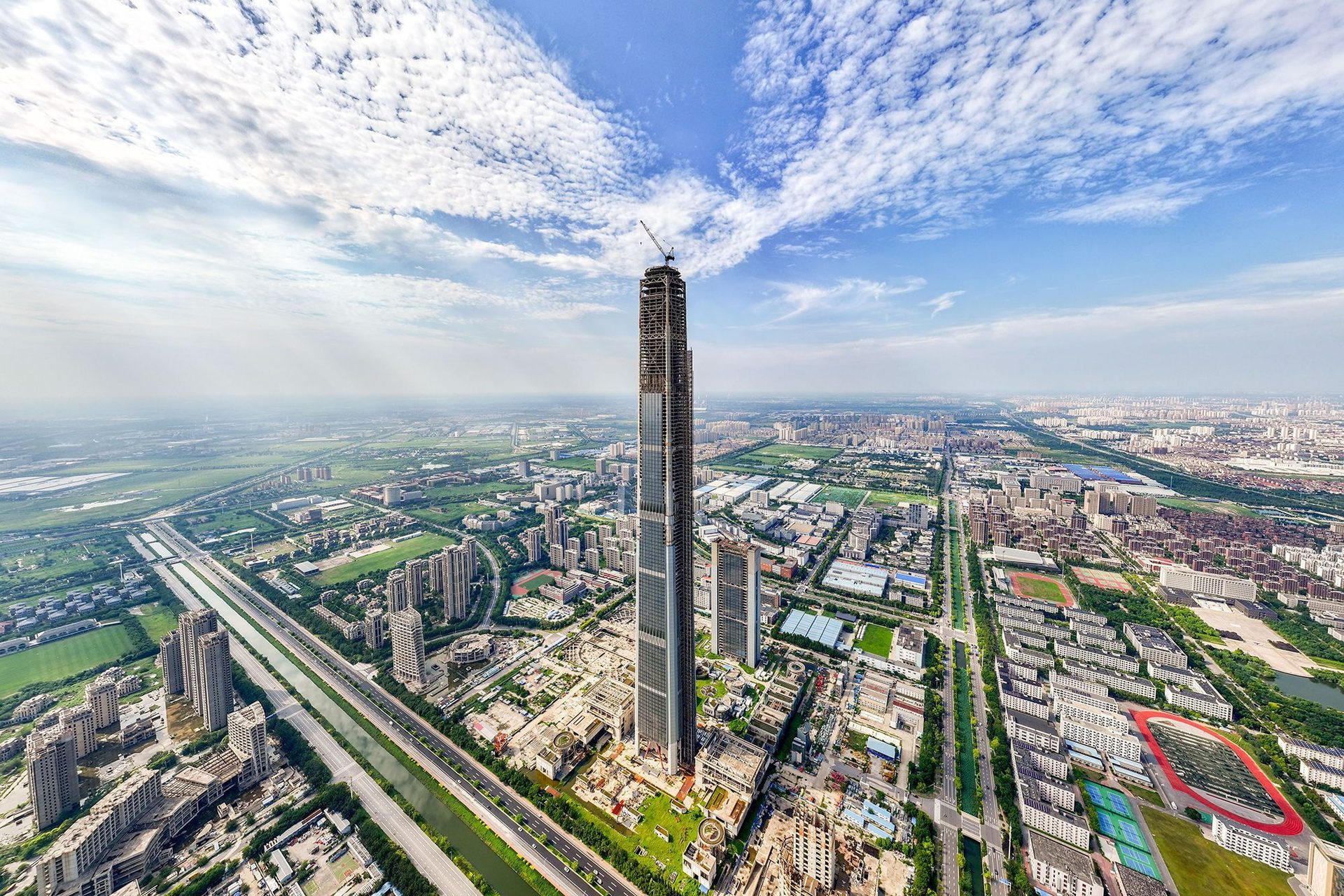 Aerial view of a sprawling city dominated by a very tall, under-construction skyscraper.