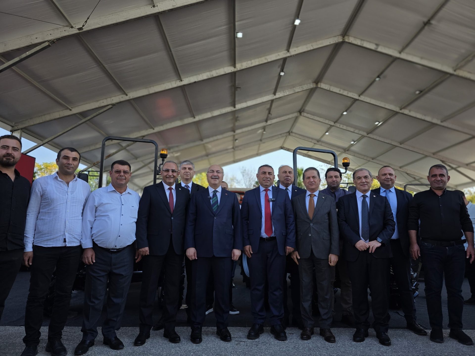 A group of men, some in suits and some in casual attire, posing under a large white tent.
