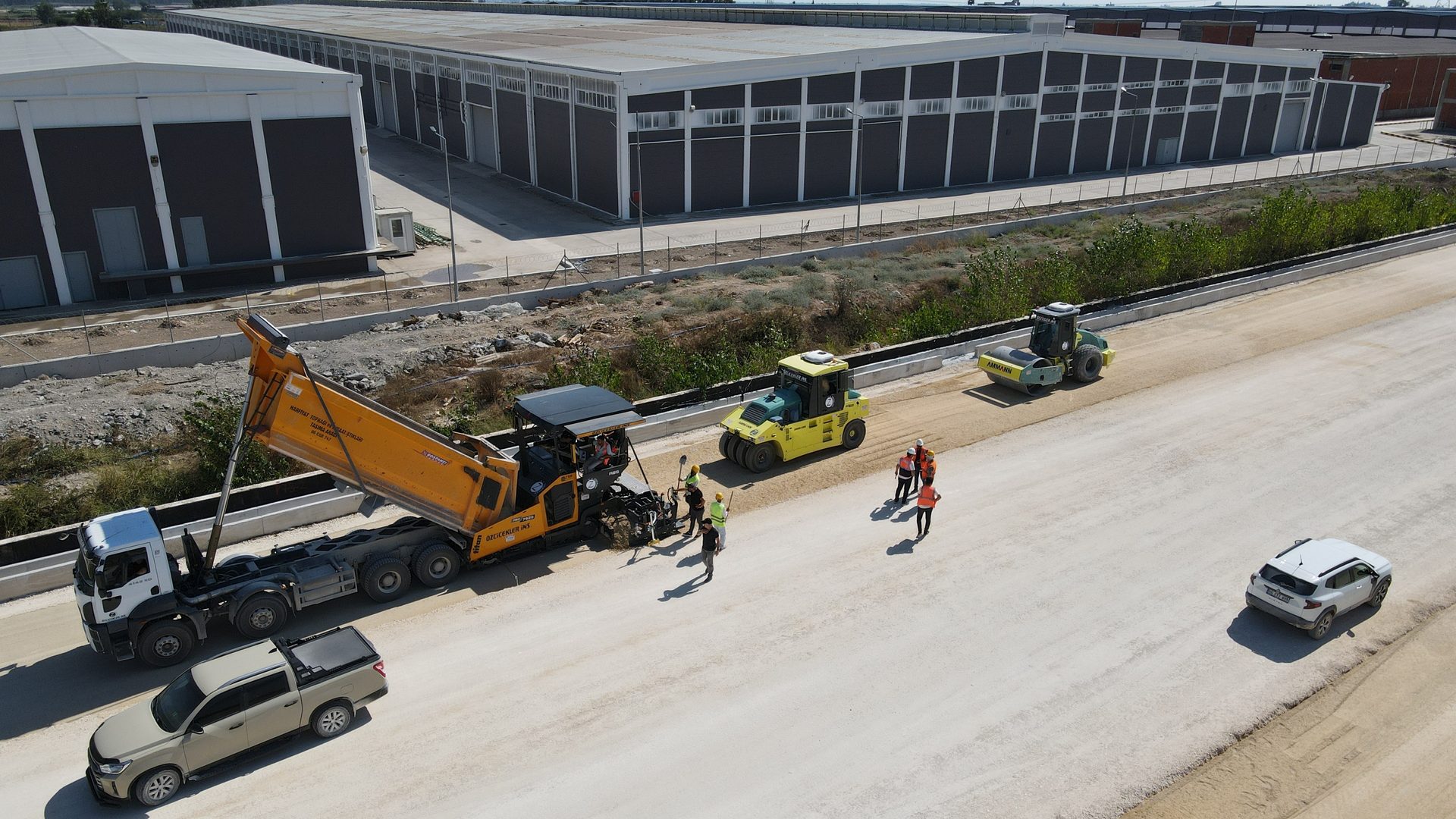 Aerial view of road construction with machinery and workers in an industrial area.