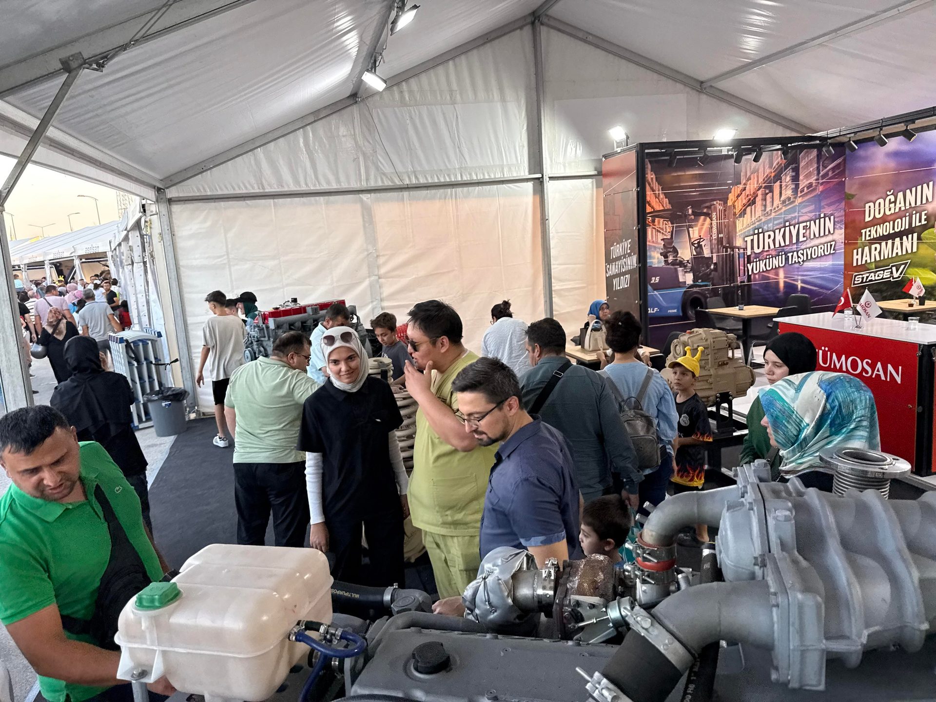 Crowded exhibition in a tent with people looking at industrial engines.