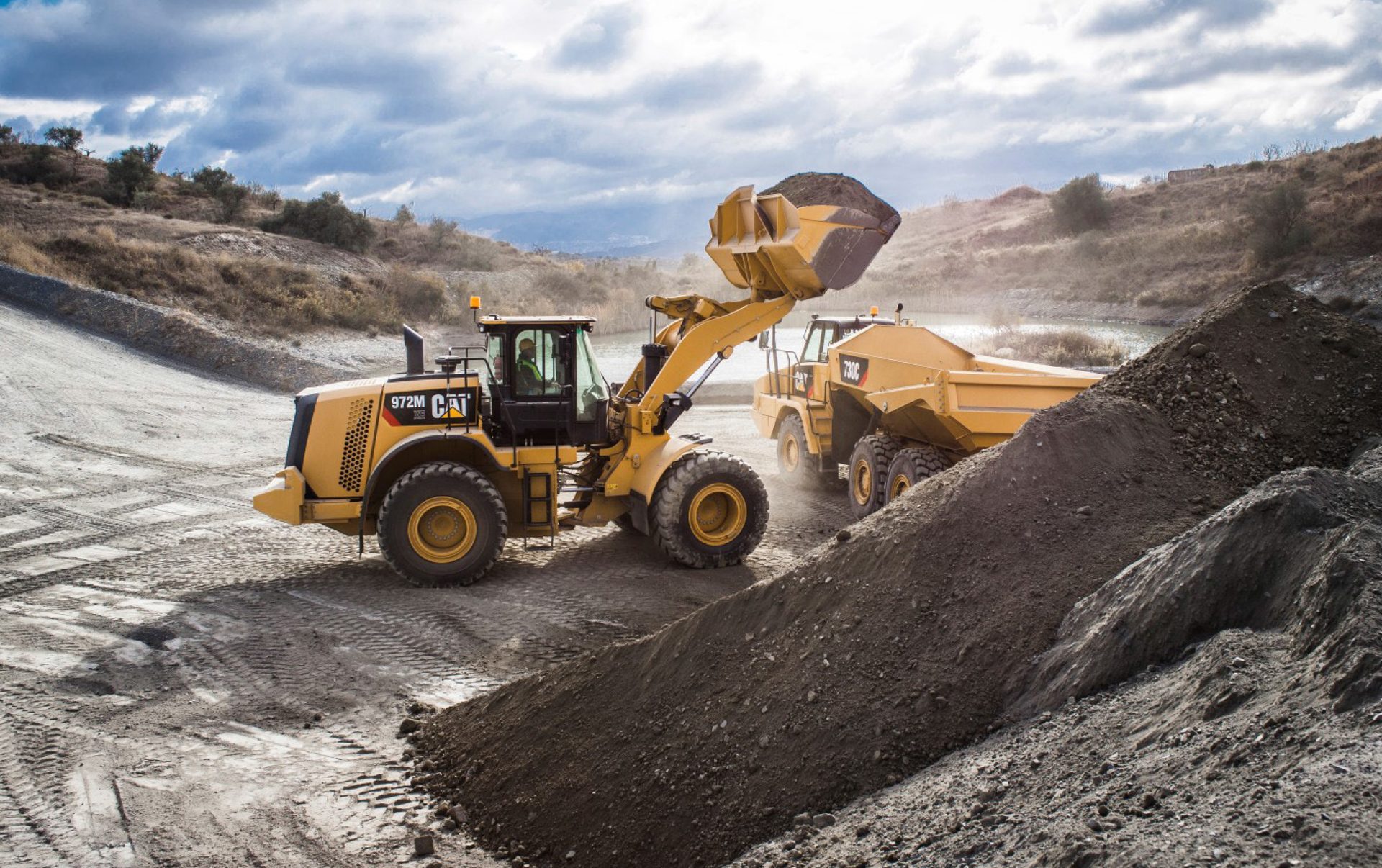 CAT 972M loader fills 730C dump truck with dirt at a quarry.