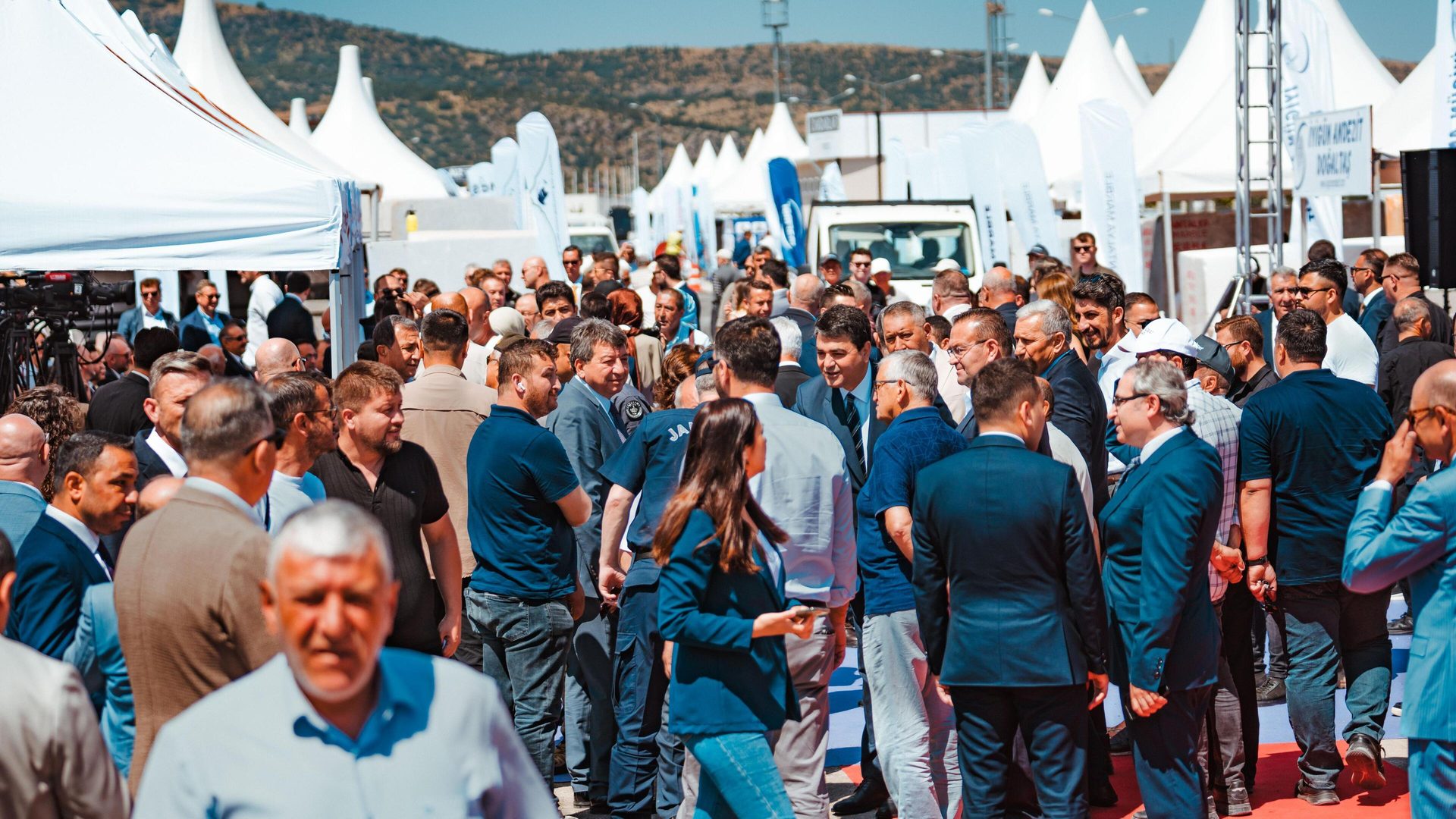 A large crowd of people at an outdoor event with white tents.