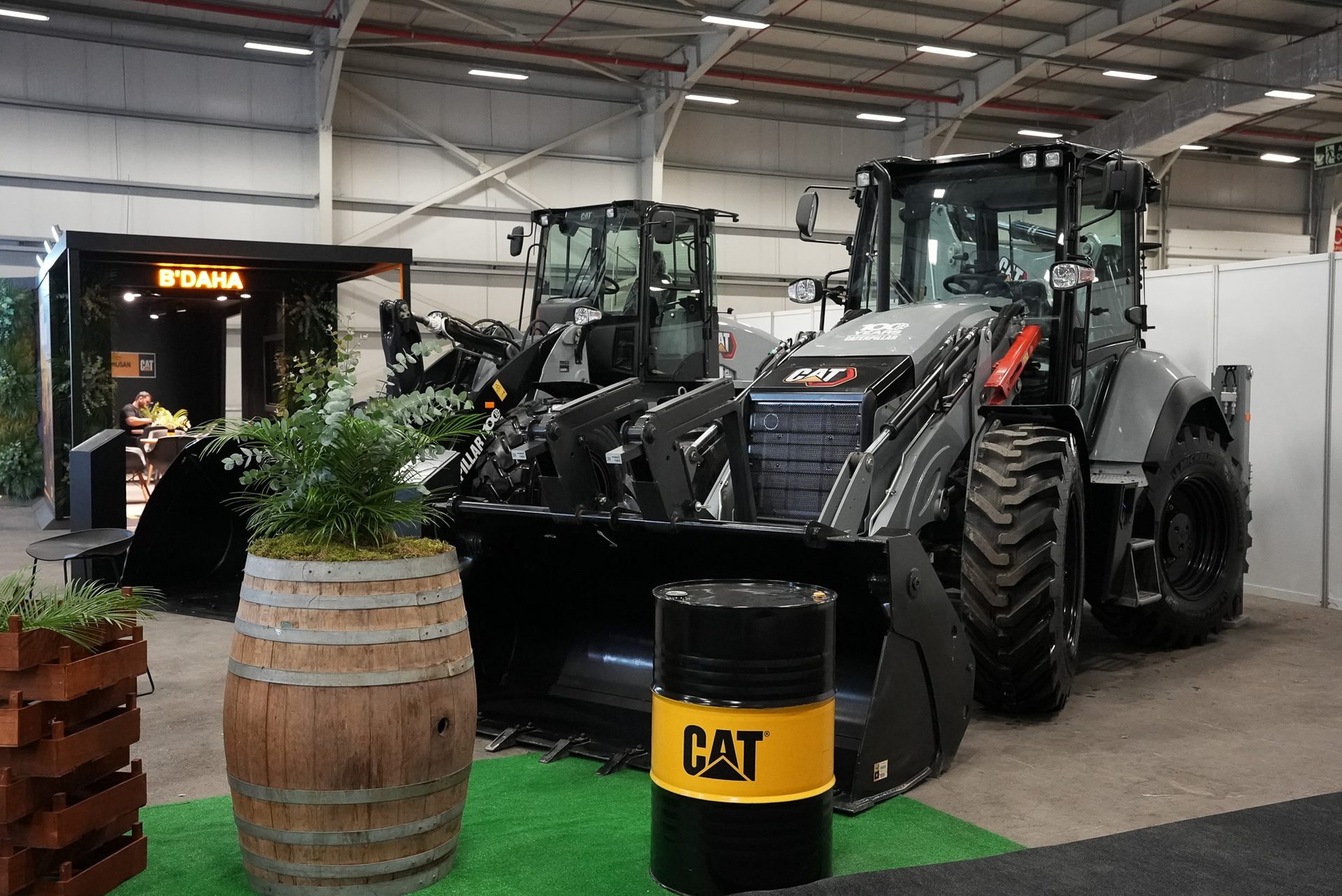 Two grey Caterpillar loaders on display at an indoor exhibition booth with a B'DAHA sign.