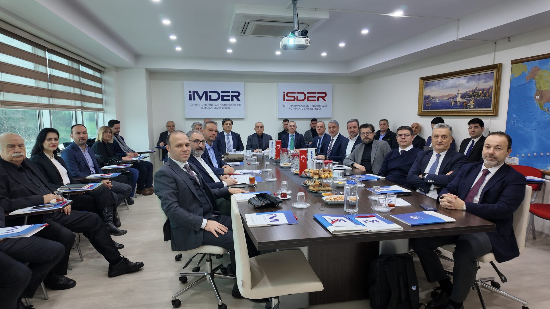 A group of professionals in suits attending a meeting around a conference table with snacks.