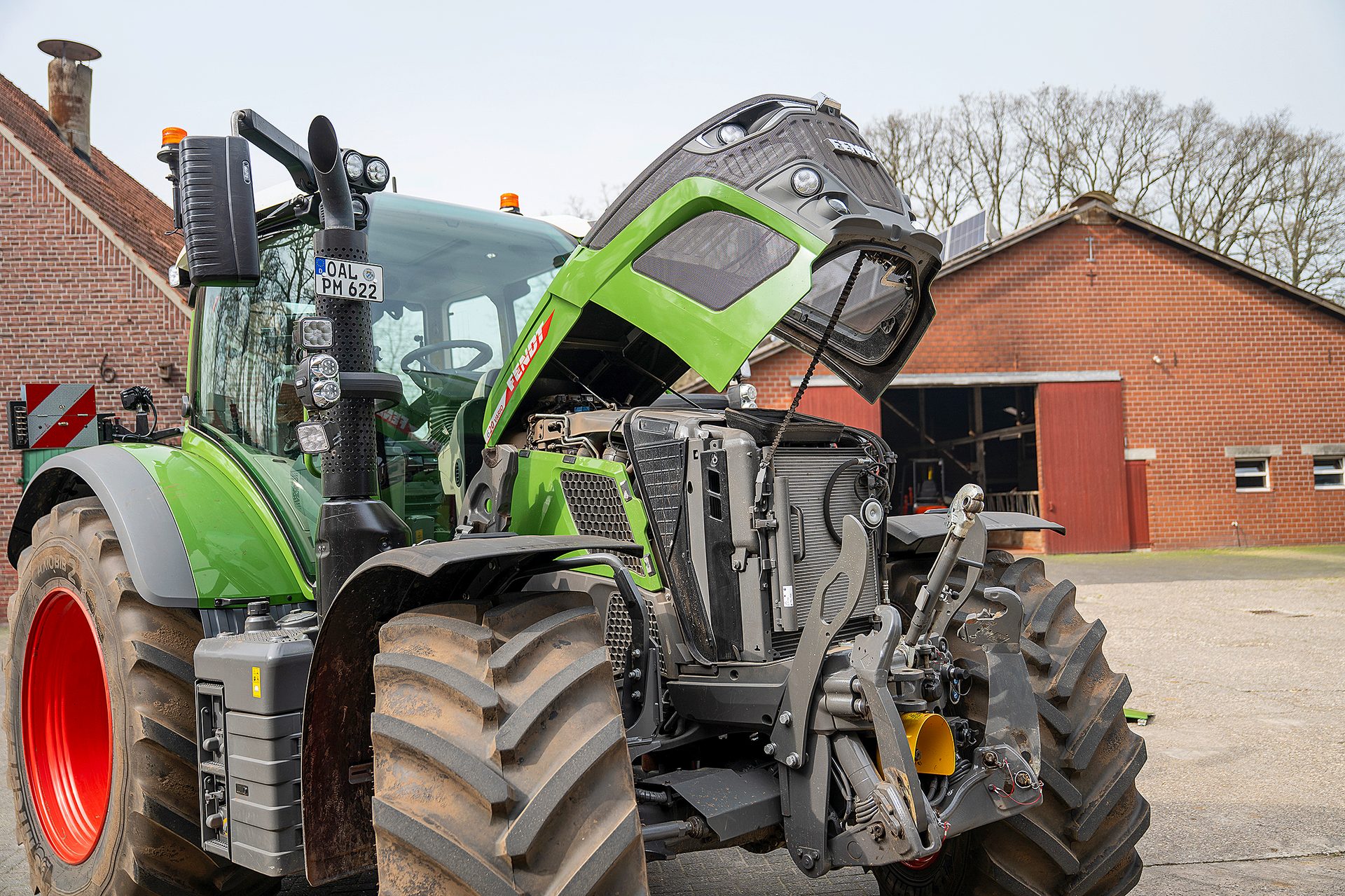 Green Fendt tractor with open hood revealing engine, parked at a farm.