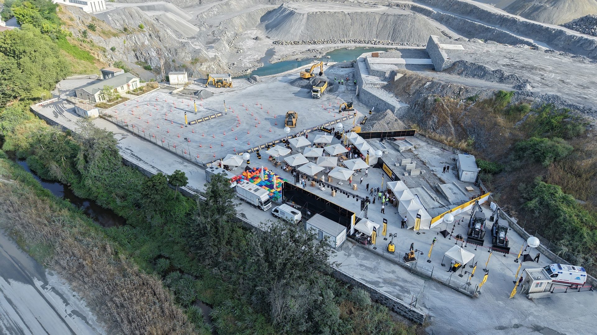 Aerial view of an outdoor event at a quarry with heavy machinery, tents, and people.