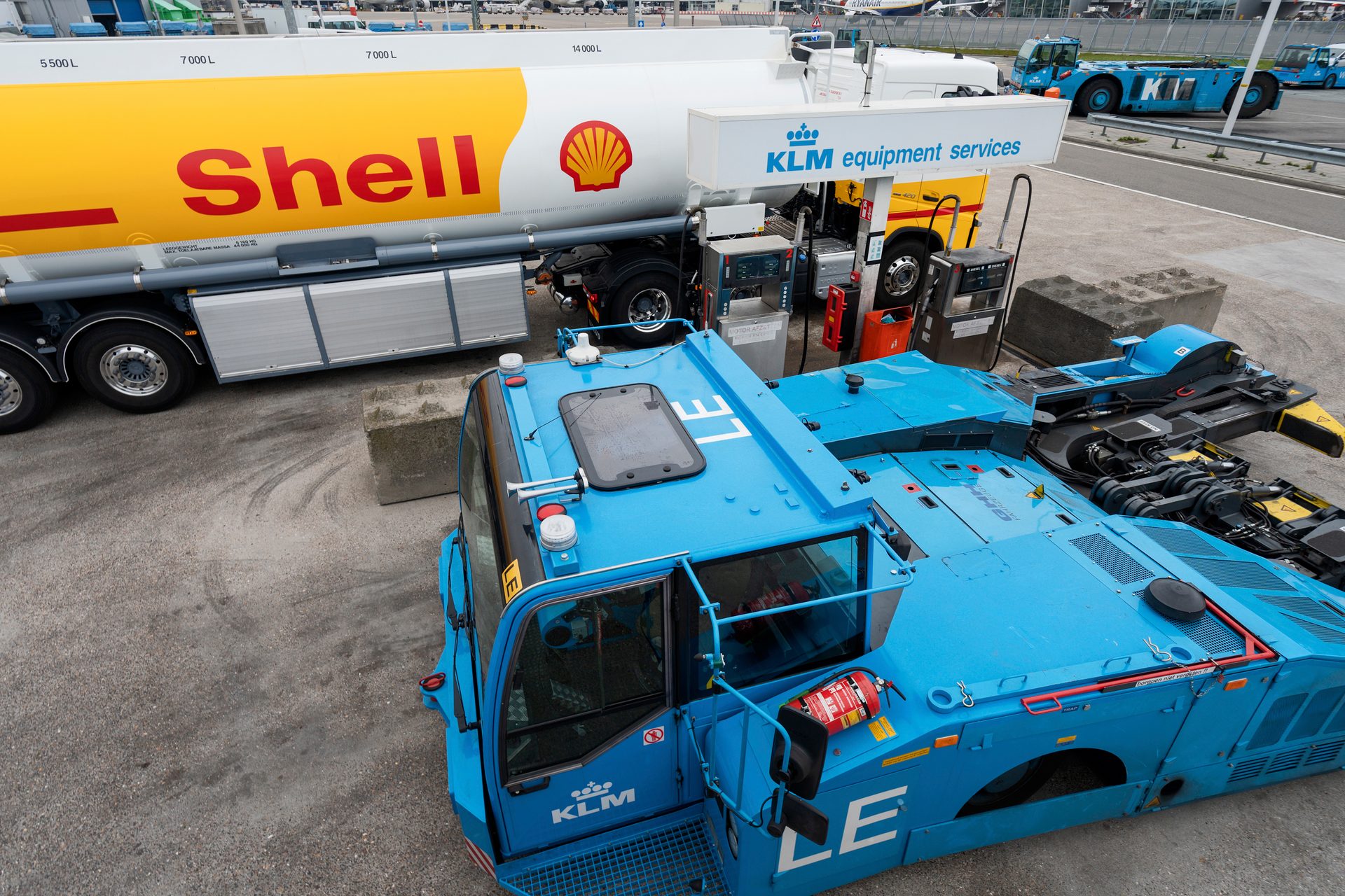 Shell fuel tanker refueling a blue KLM equipment vehicle at an airport.