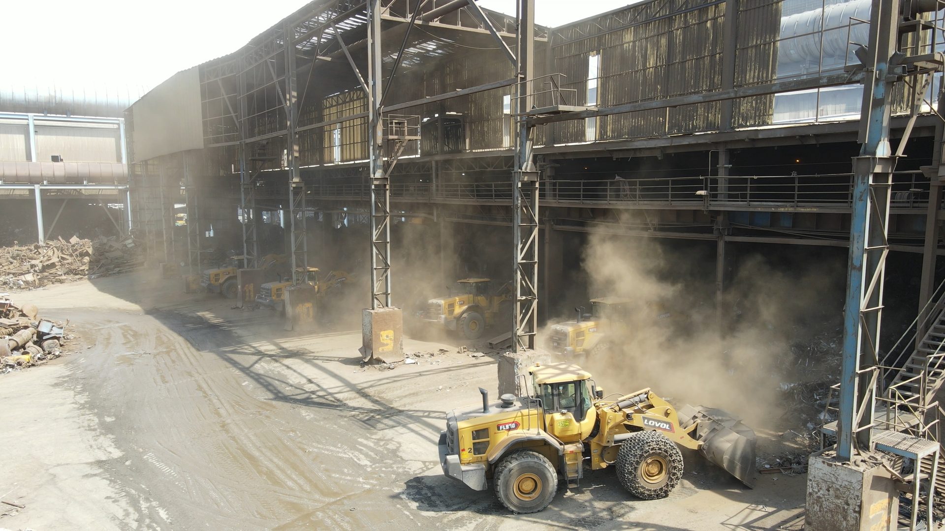Yellow LOVOL front-end loaders move scrap metal in a very dusty industrial building.