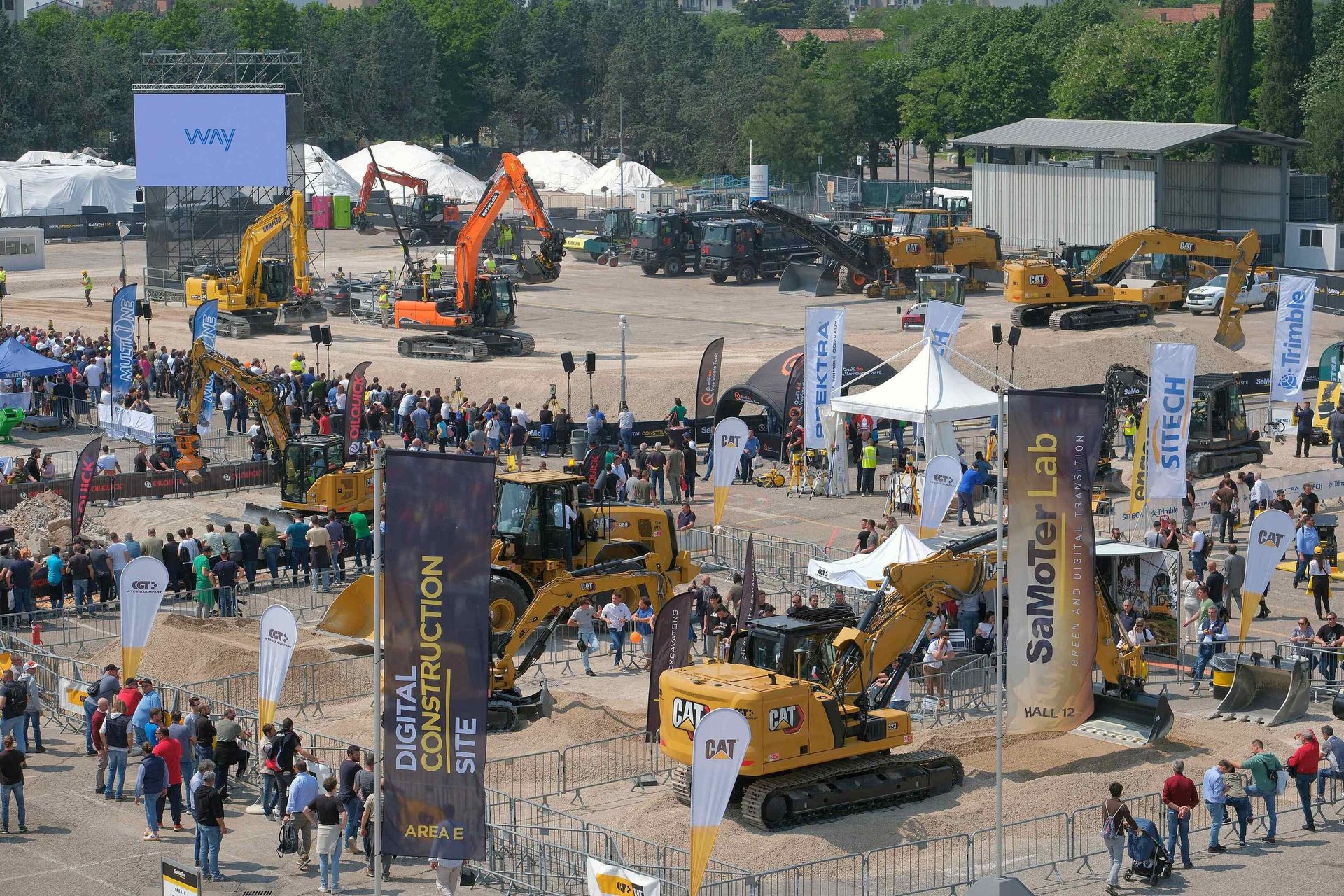 Large outdoor construction machinery exhibition with excavators, people, and industry tech displays.