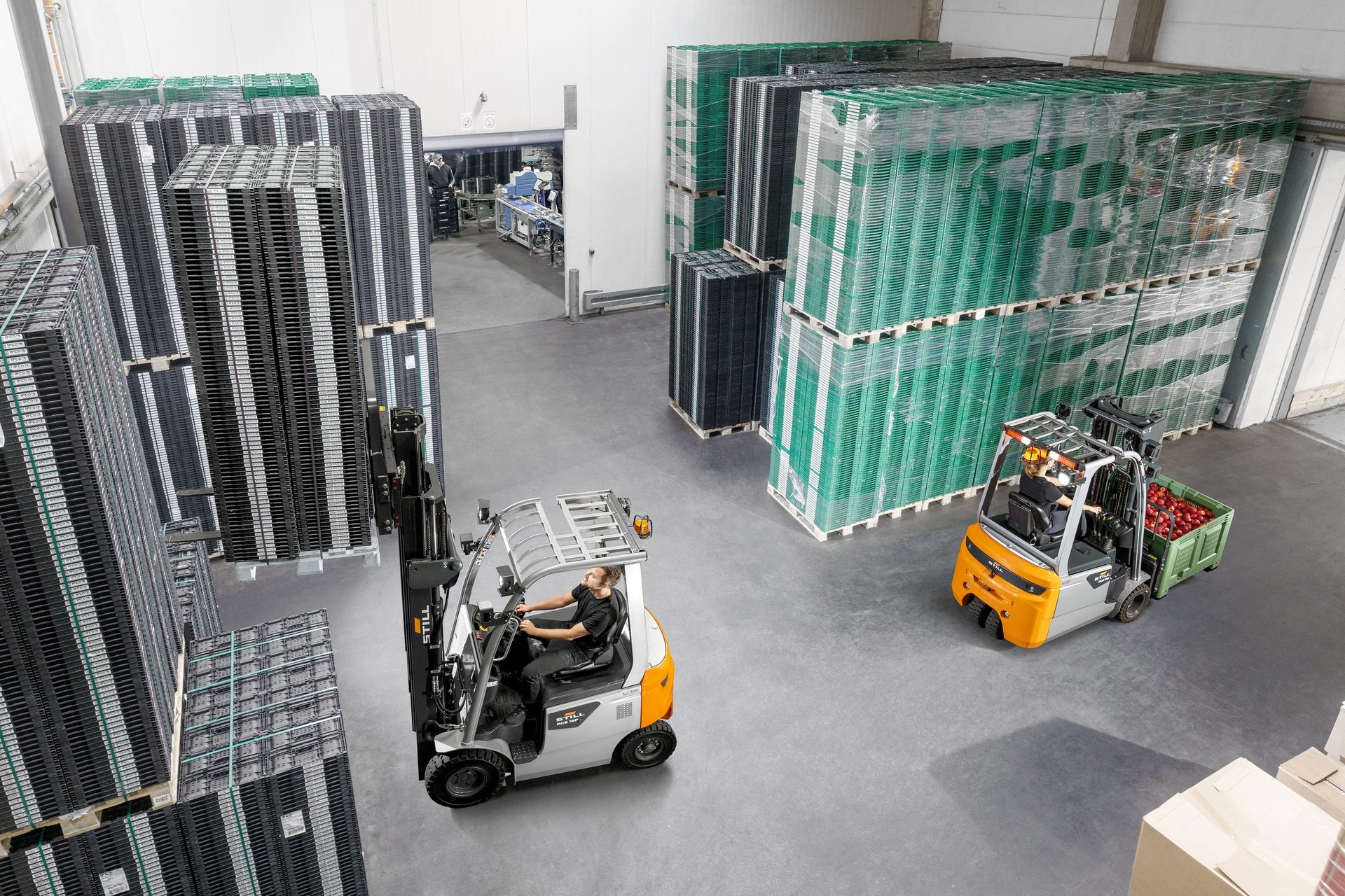 Warehouse scene with forklifts moving stacked crates and apples.