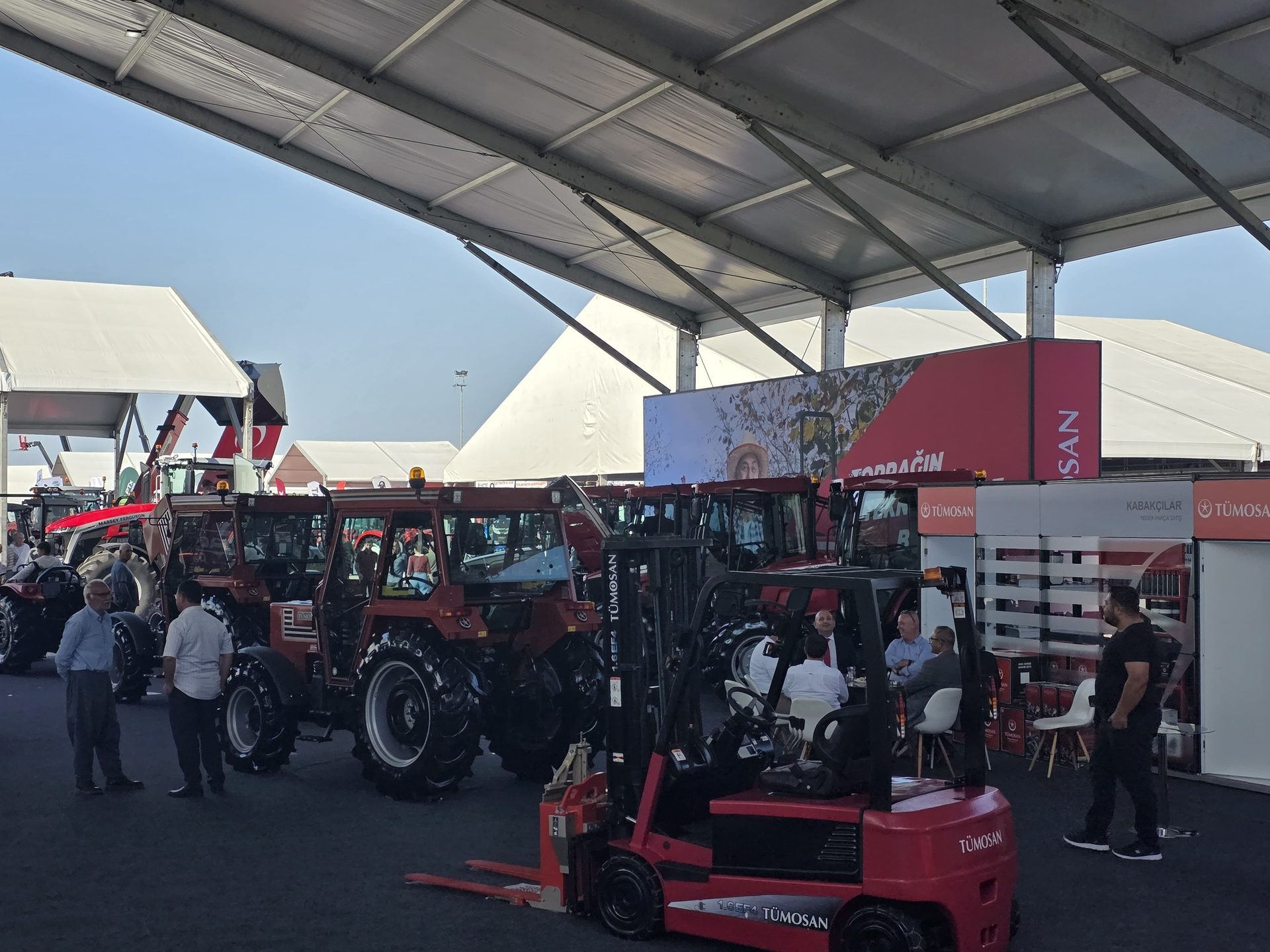 TÜMOSAN tractors and a forklift displayed at an outdoor agricultural exhibition with attendees.