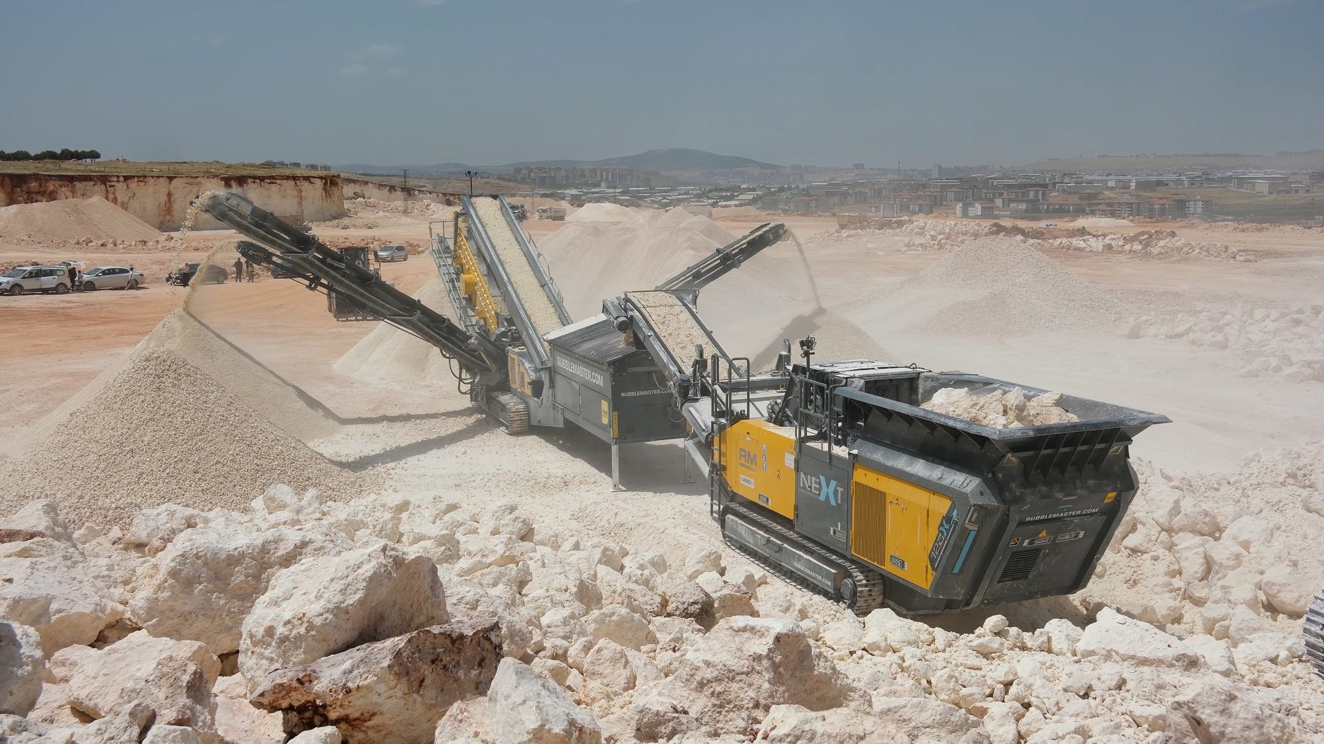 Mobile rock crushers and screening plants operating in a dusty white stone quarry.