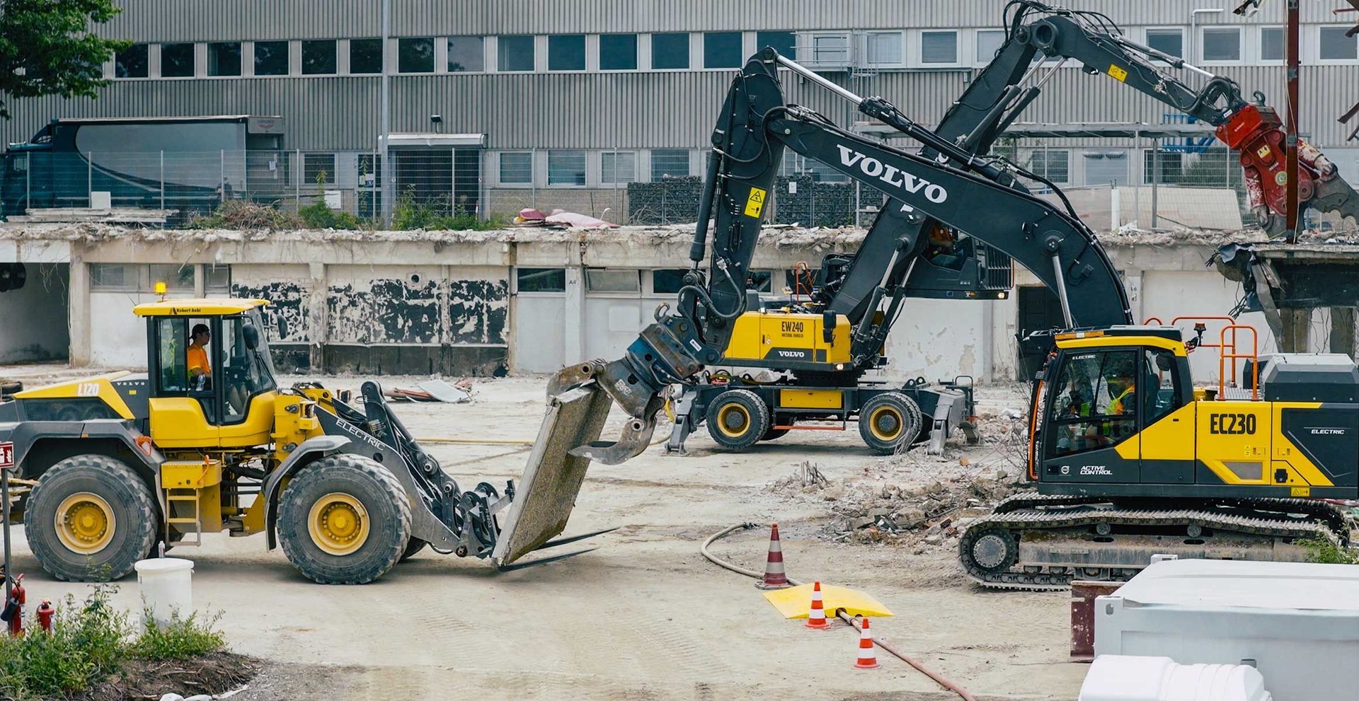 Three electric Volvo excavators and a wheel loader operate at a demolition site.