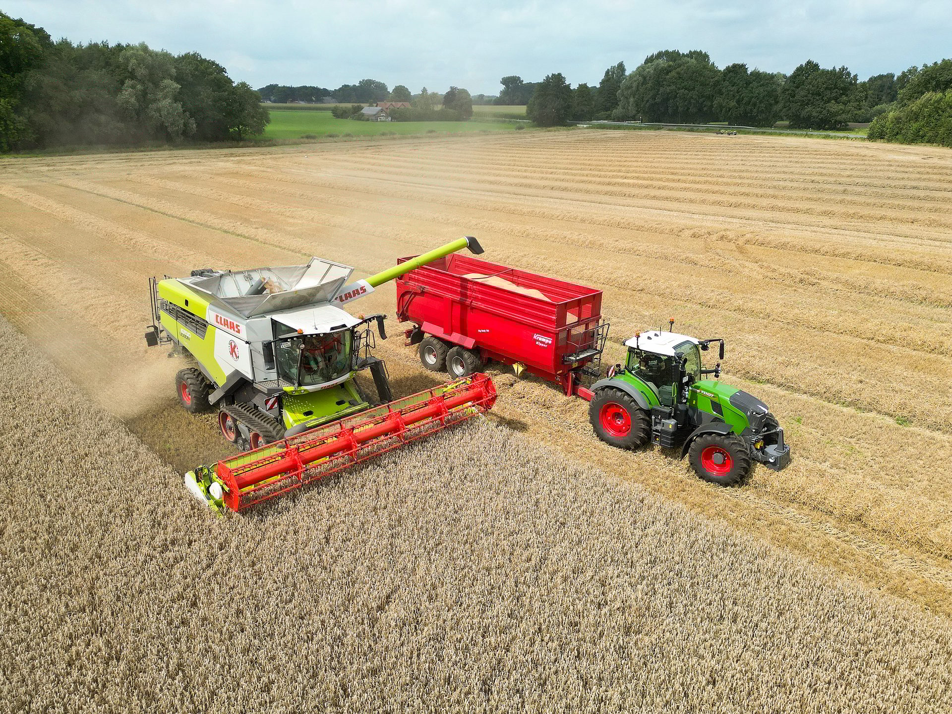Combine harvester offloads grain into a tractor-pulled trailer in a wheat field.