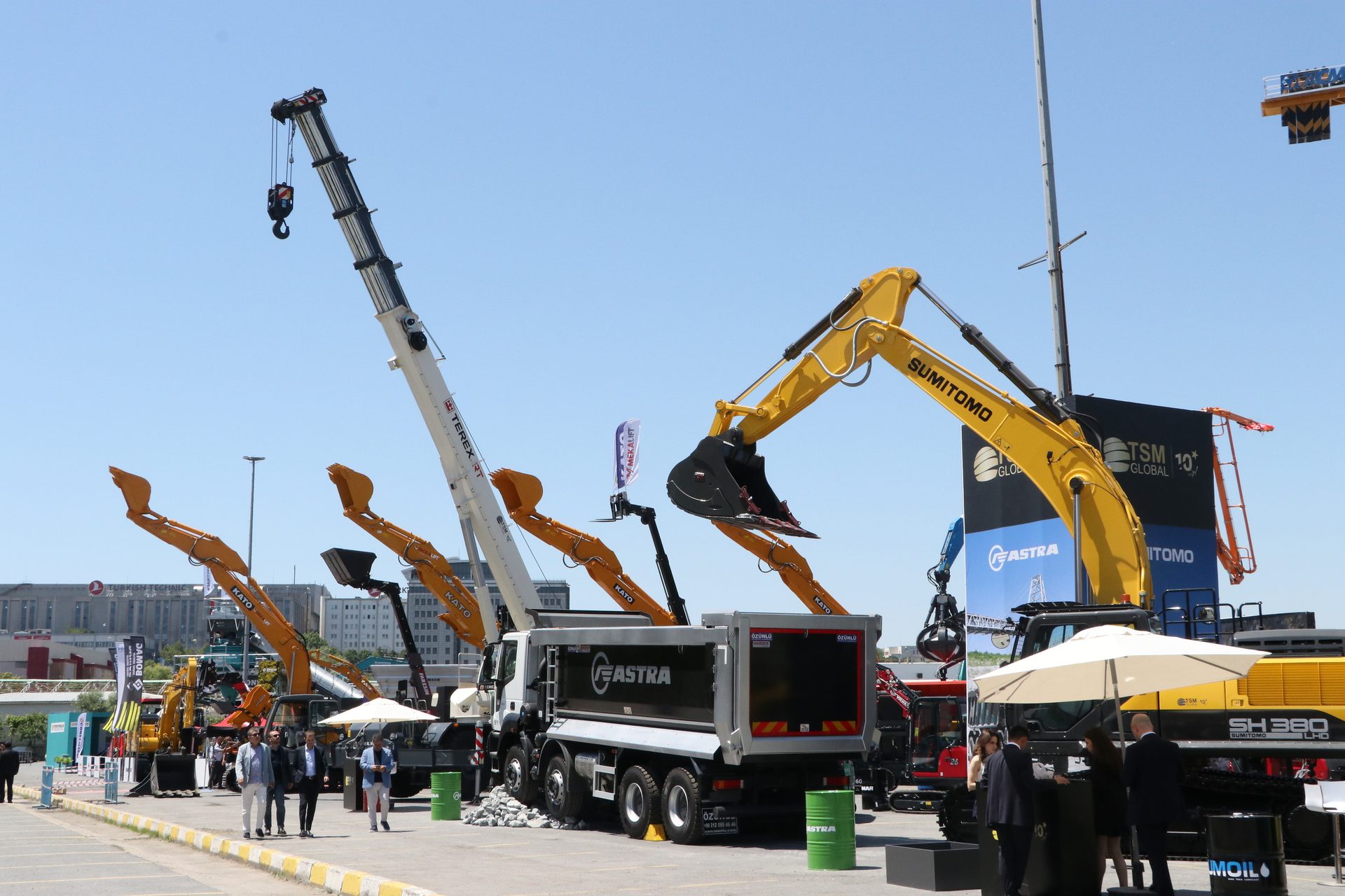 Construction machinery exhibition with Terex crane, Sumitomo excavators, and Fastra truck.
