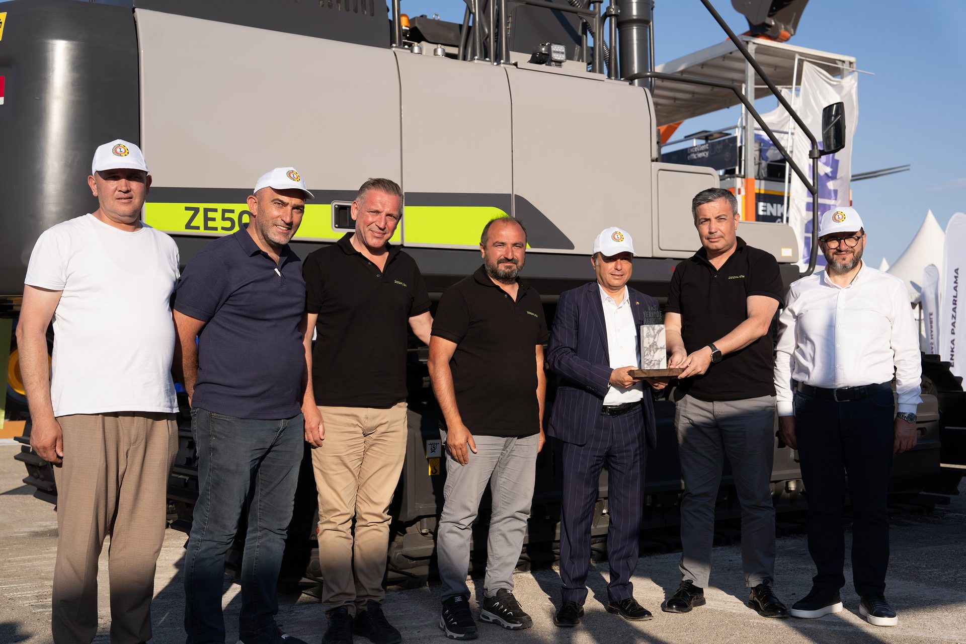 Men in caps holding an award in front of a ZE50 construction machine.