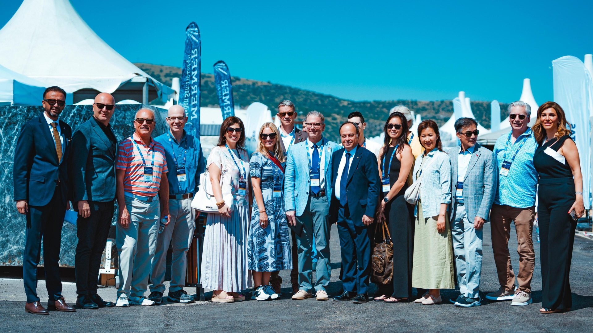 A diverse group of people posing outdoors at a sunny event with white tents.