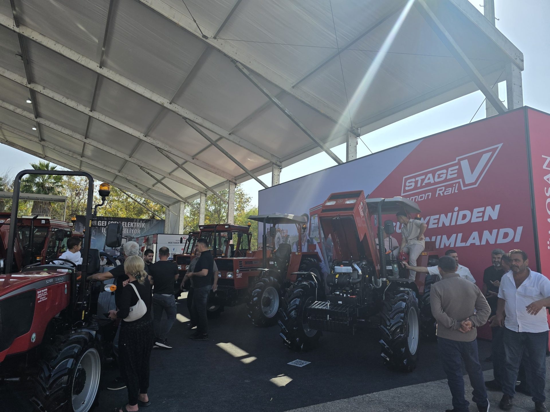 People viewing red Stage V TUMOSAN tractors at an exhibition under a tent.