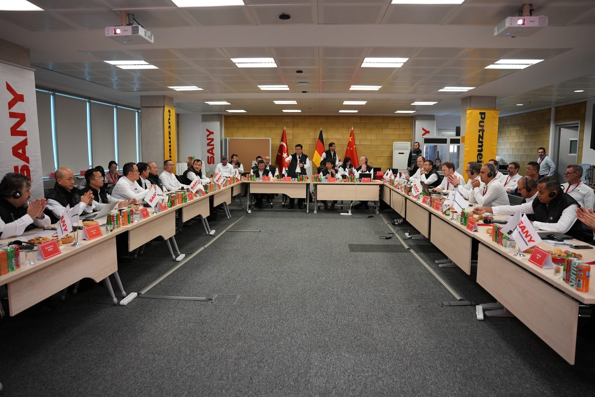 People attend an international business meeting in a conference room with SANY banners and national flags.