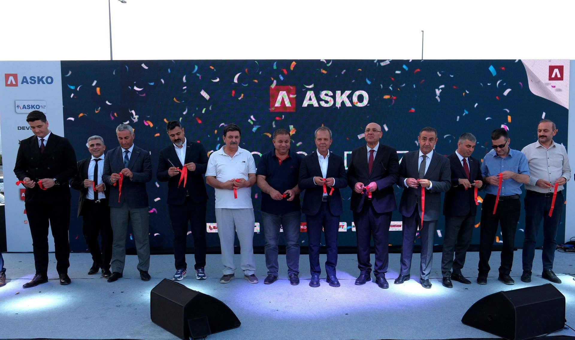 Men cutting red ribbons on stage in front of an ASKO screen with confetti.