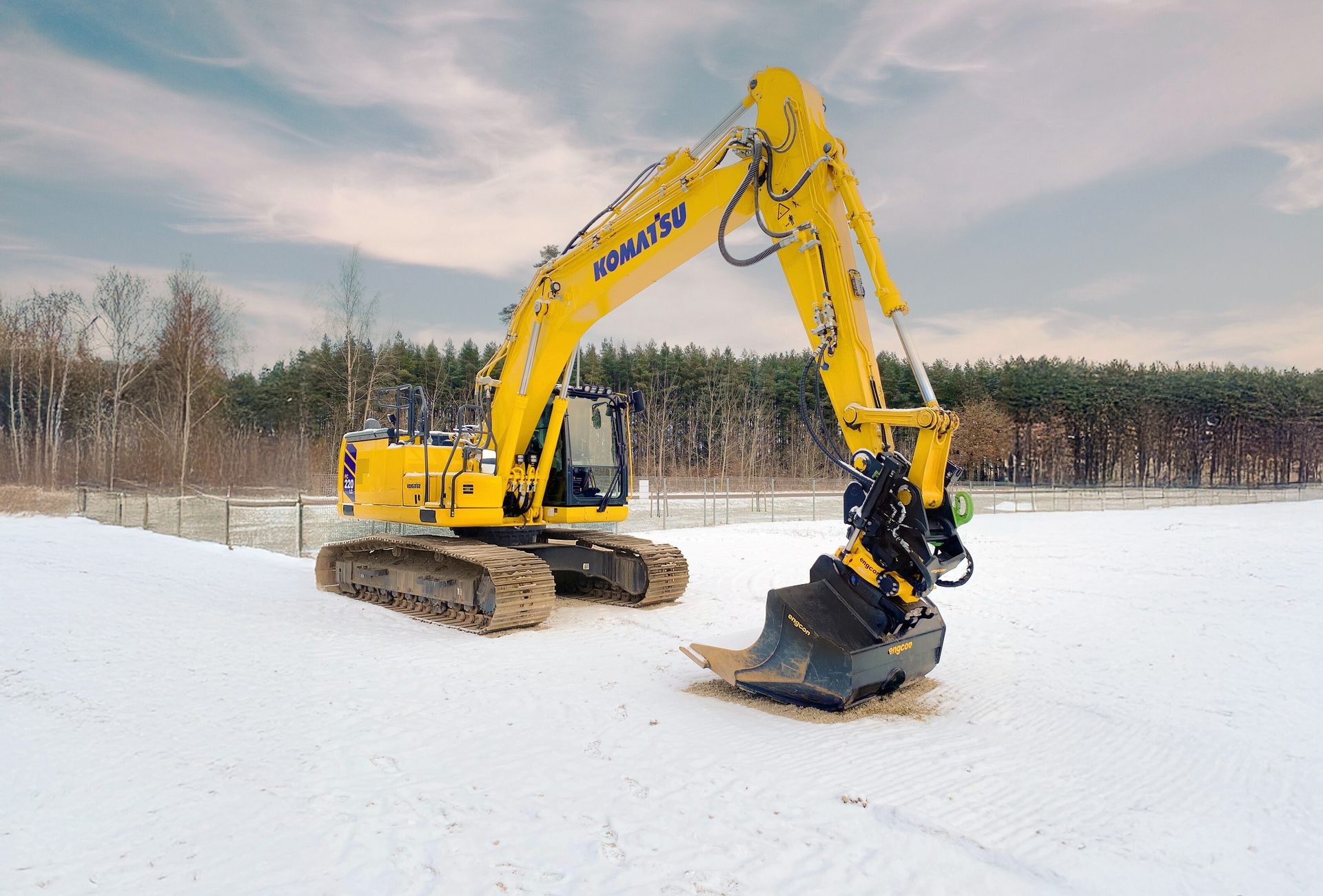 Yellow Komatsu excavator in a snowy field with trees in the background.