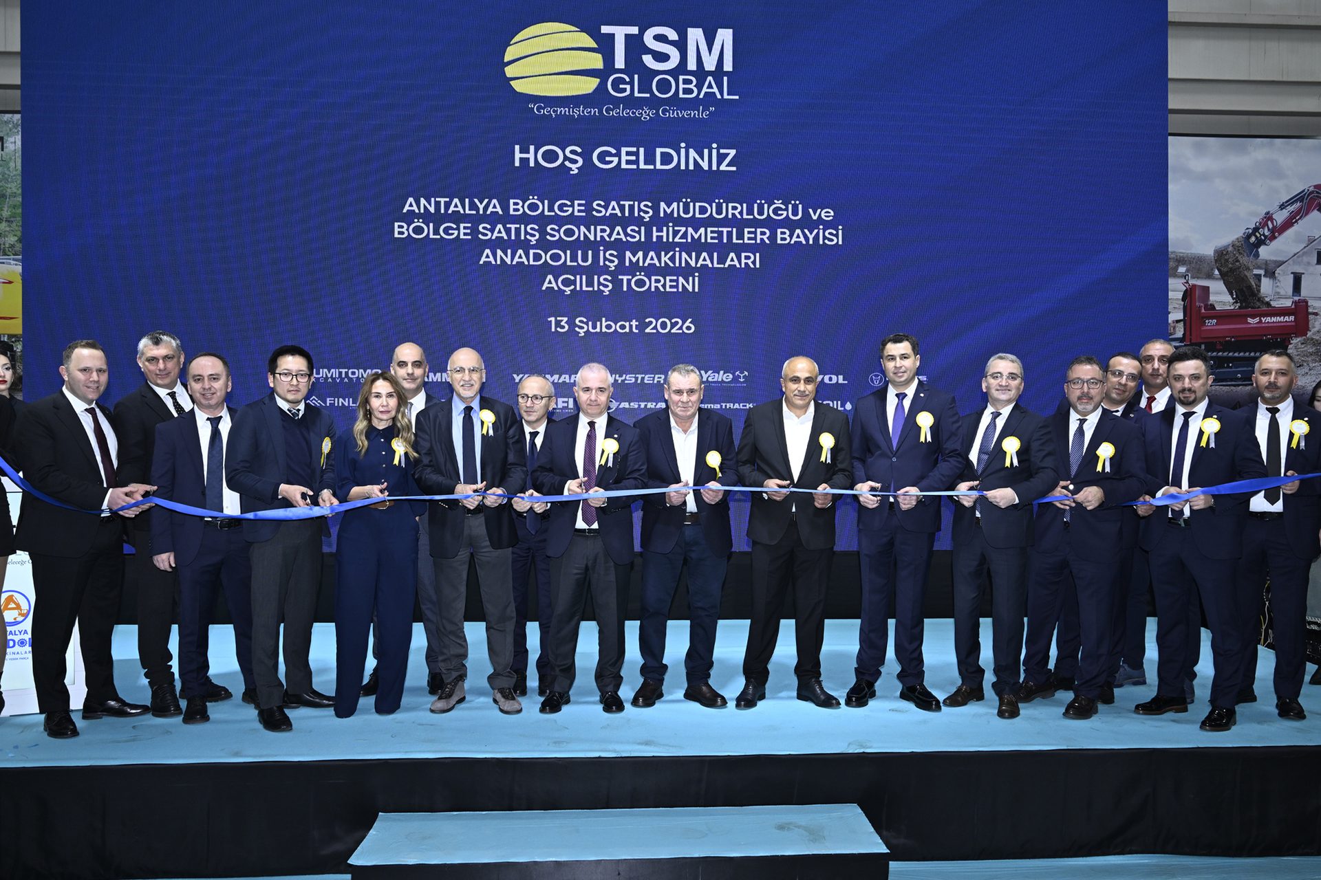 A group of people in suits are cutting a blue ribbon at an opening ceremony in front of a large digital screen.