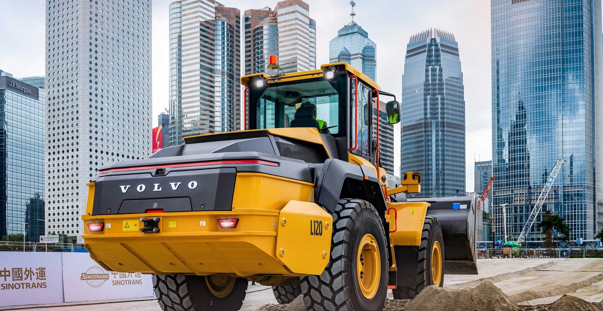 Yellow Volvo loader at a construction site with city skyscrapers in the background.