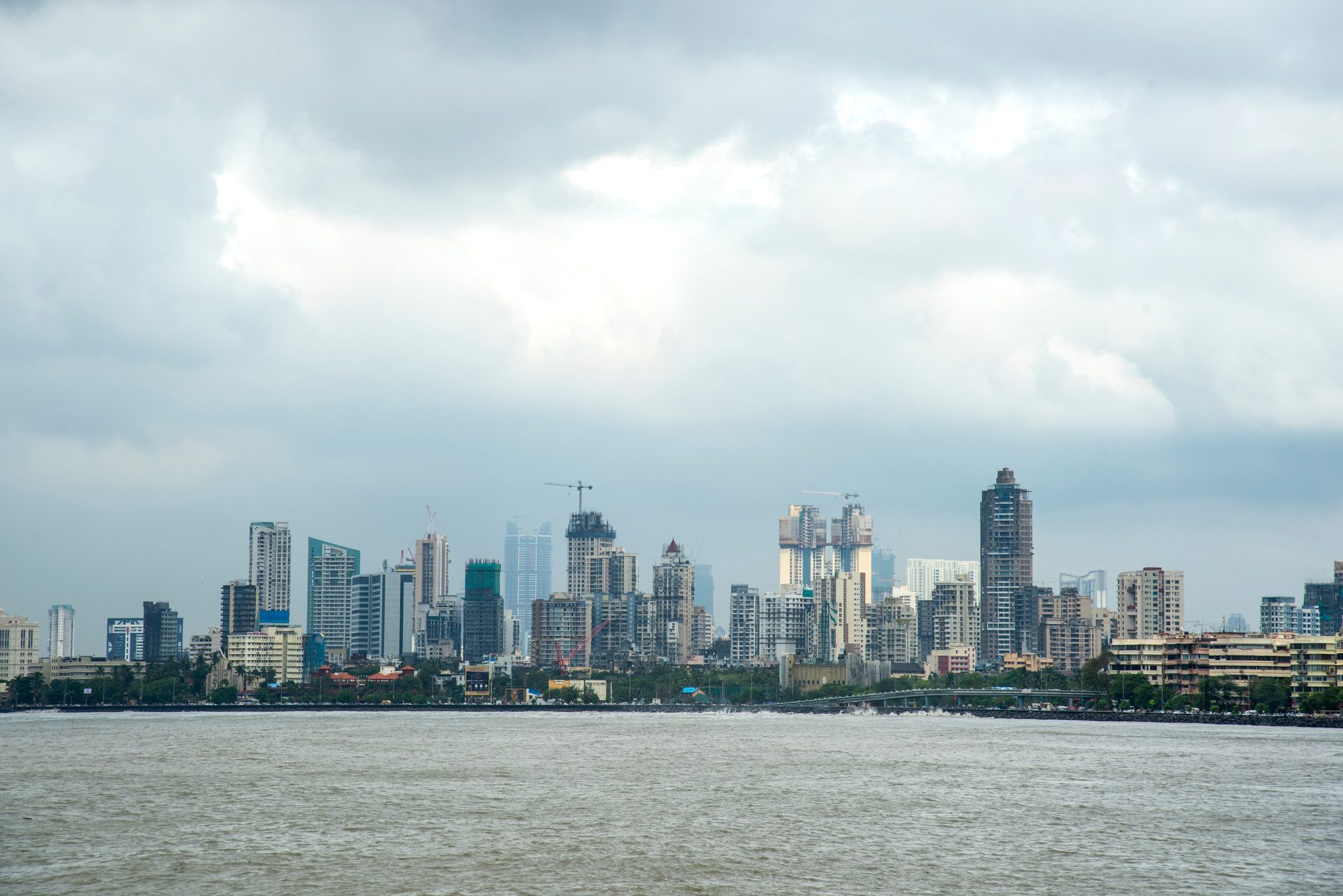 City skyline with buildings, construction, and water under cloudy sky.